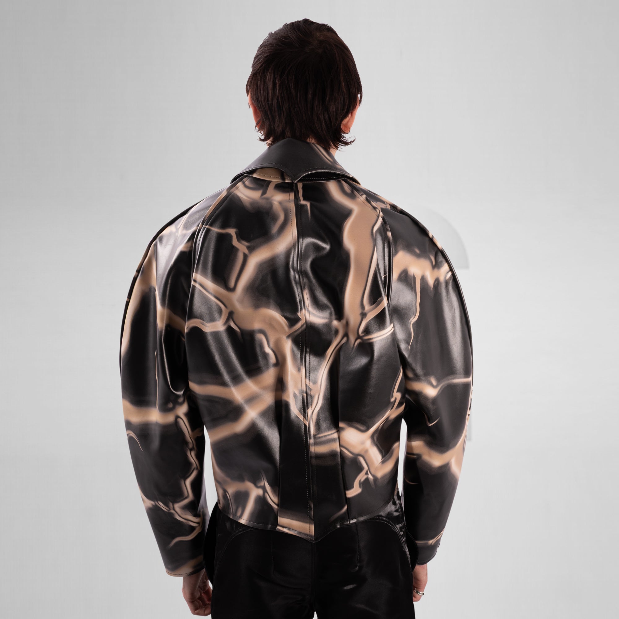 Person wearing a black and gold patterned jacket on a gray background