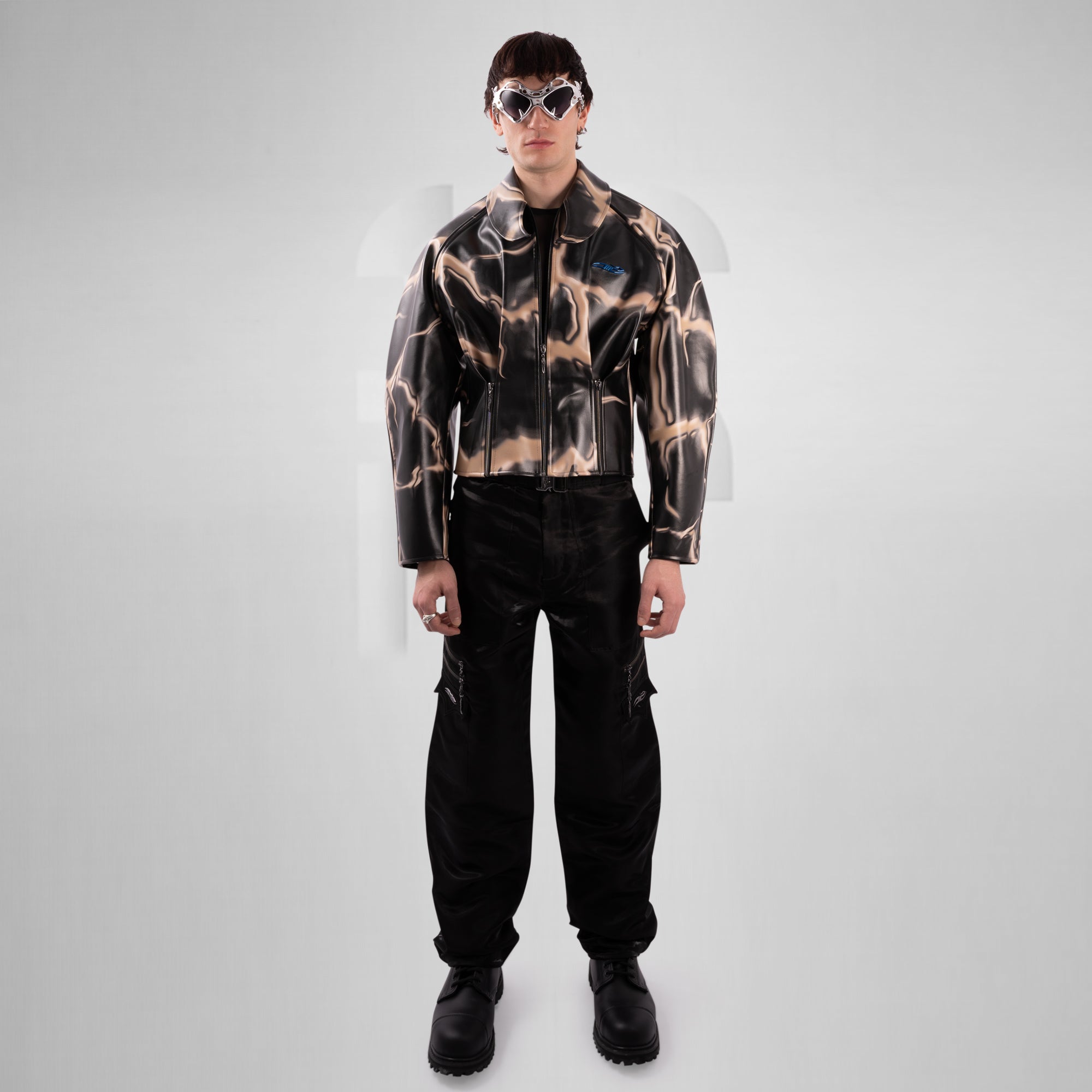 Person wearing a patterned jacket and black pants on a gray background