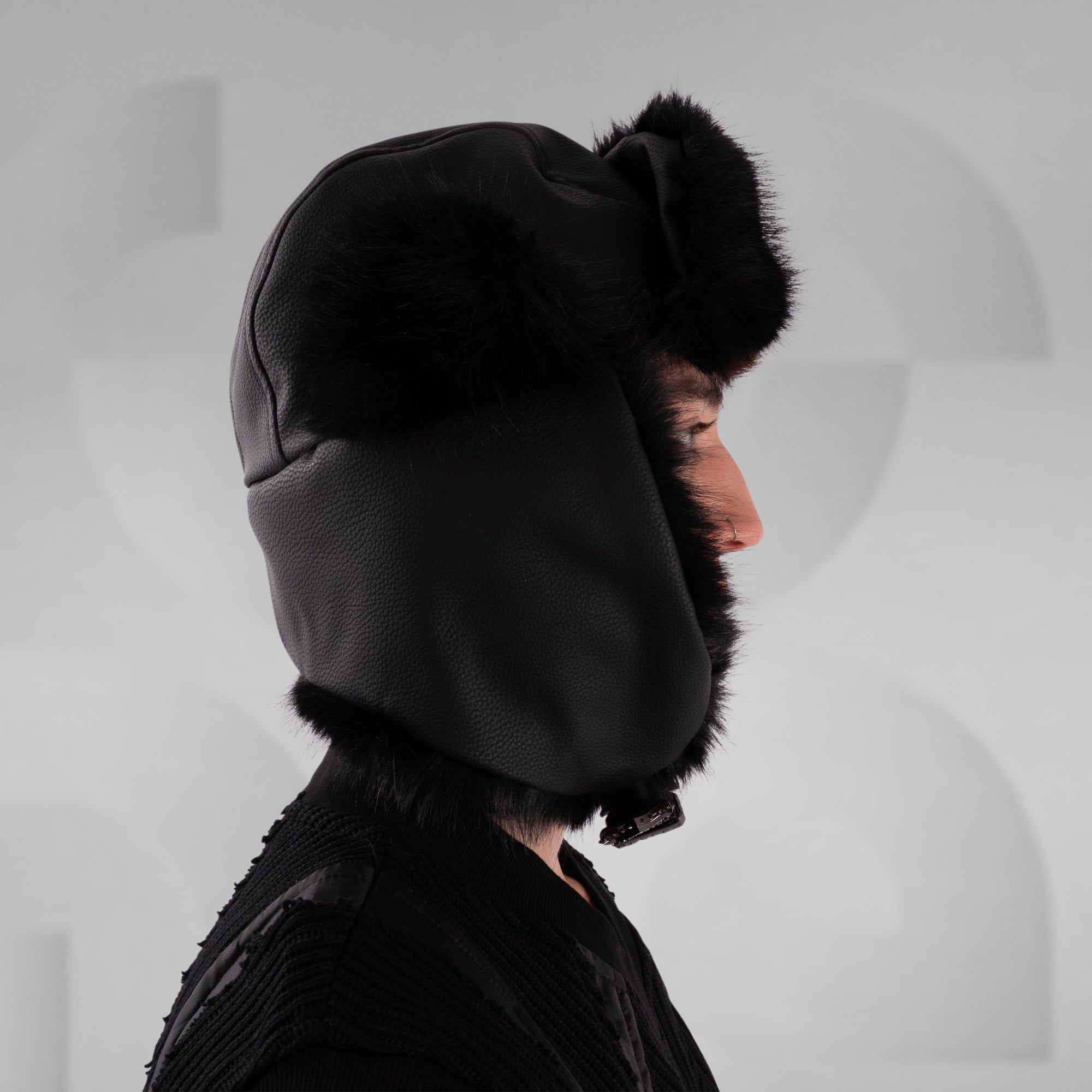 Person wearing a black winter hat with fur trim on a light gray background