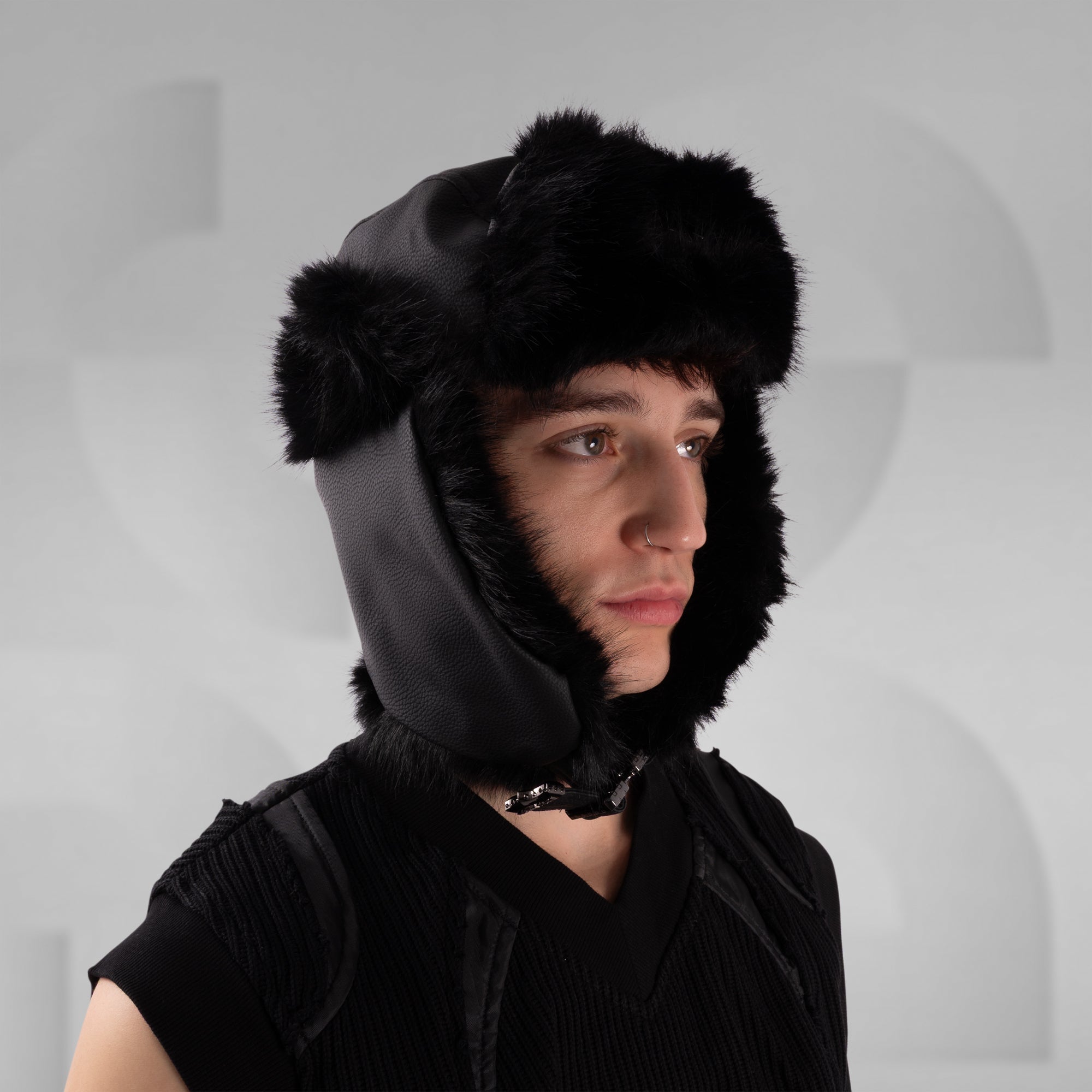 Person wearing a black fur-trimmed hood against a gray background