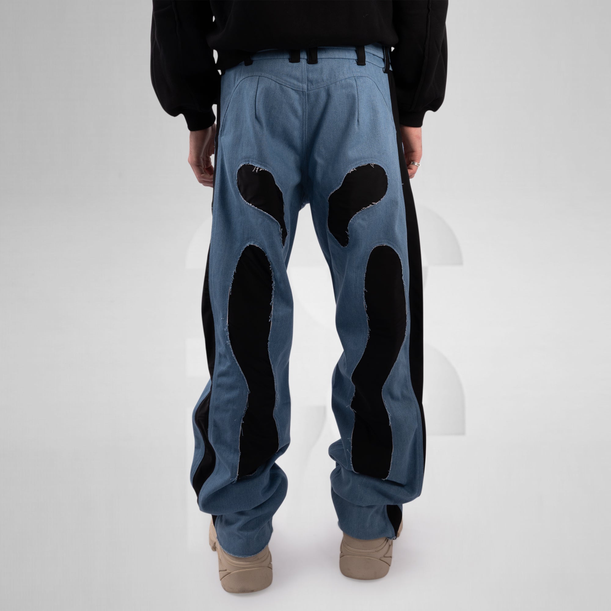 Person wearing blue pants with black patches on a white background