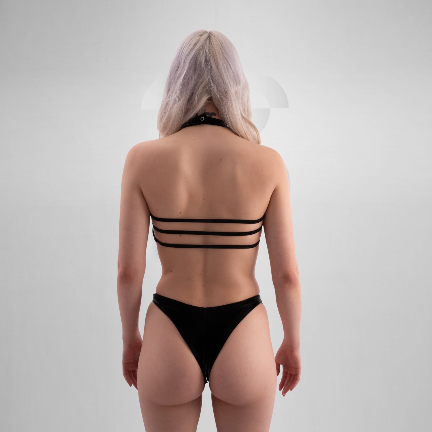 The image shows a person wearing a bold, black cut-out bodysuit. The design is sleek and daring, featuring a unique arrangement of fabric that creates striking geometric shapes on the body. 