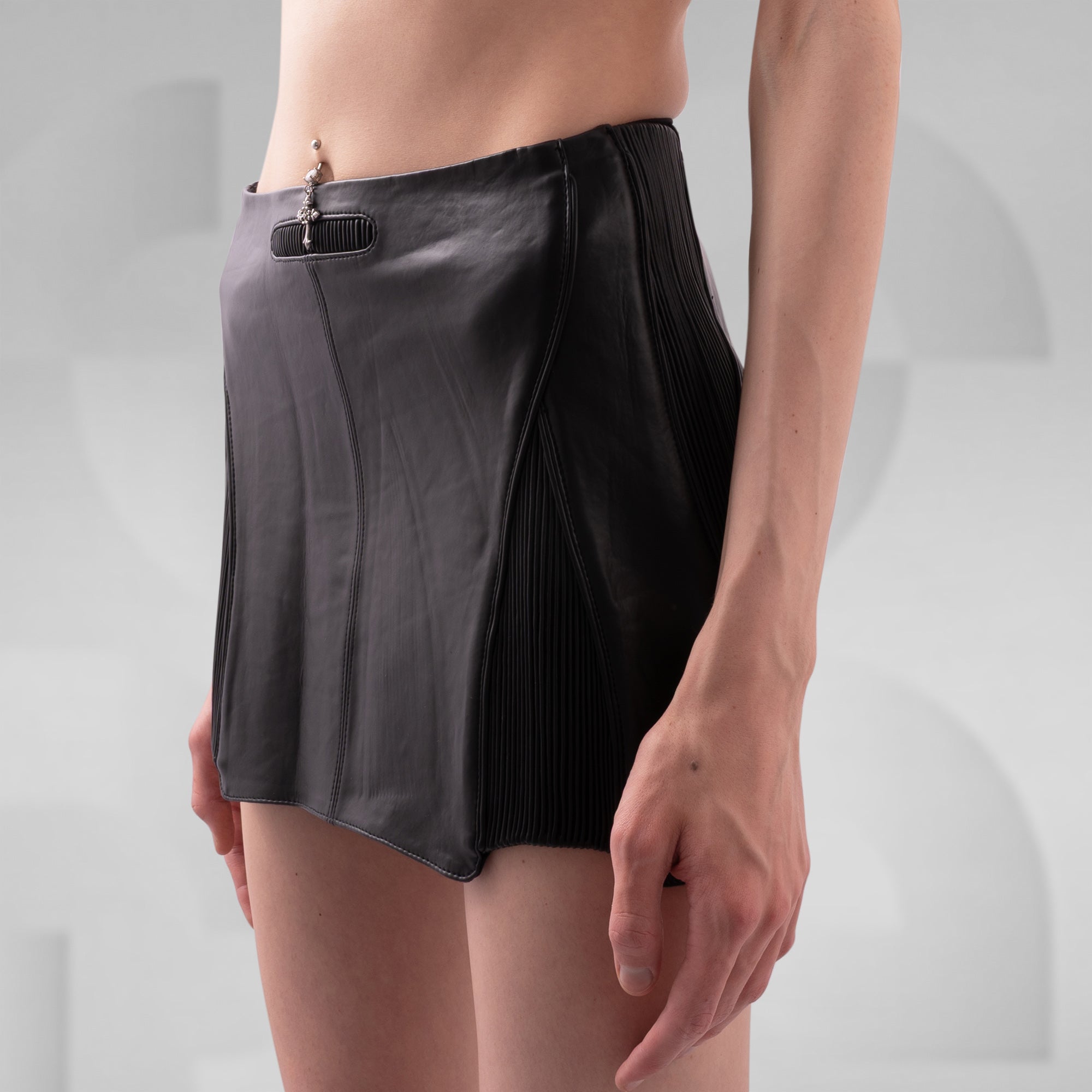 Person wearing a black pleated skirt against a plain background