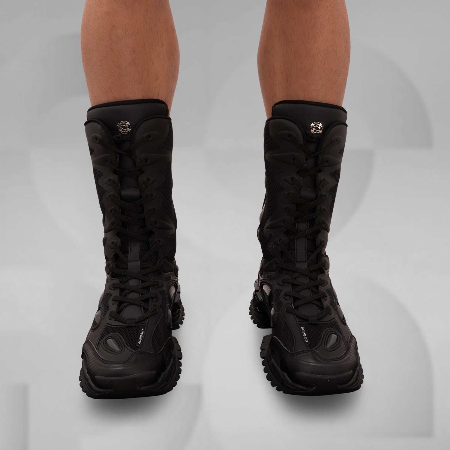 The image features the bold and avant-garde high-top boots from Rombaut, designed for a striking look. These distinctive black boots combine a rugged aesthetic with innovative details, including dynamic lacing and textural contrasts. Ideal for making a statement in any clubwear repertoire, they elevate your style with a perfect blend of functionality and high fashion. Perfect for those who dare to stand out!