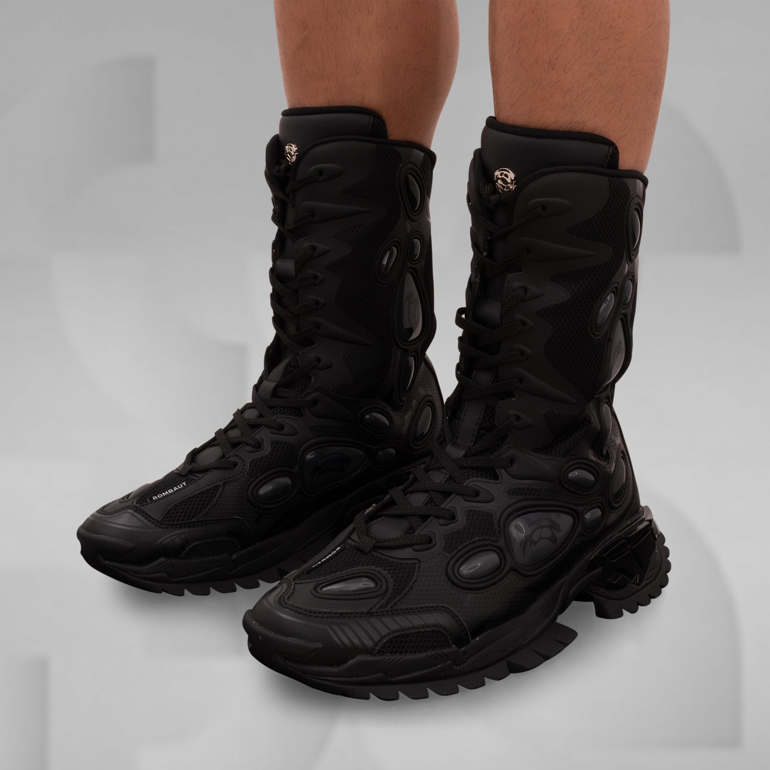 The image features the bold and avant-garde high-top boots from Rombaut, designed for a striking look. These distinctive black boots combine a rugged aesthetic with innovative details, including dynamic lacing and textural contrasts. Ideal for making a statement in any clubwear repertoire, they elevate your style with a perfect blend of functionality and high fashion. Perfect for those who dare to stand out!