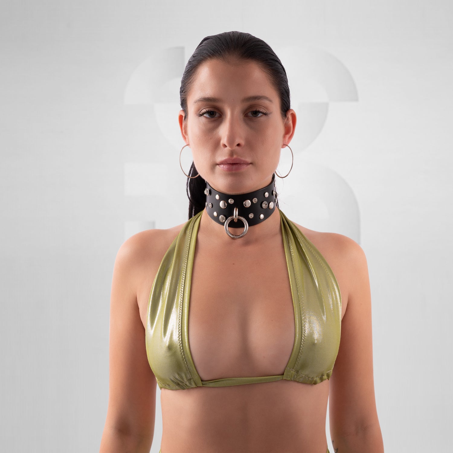 Woman wearing a green bikini top with a black studded choker against a white background