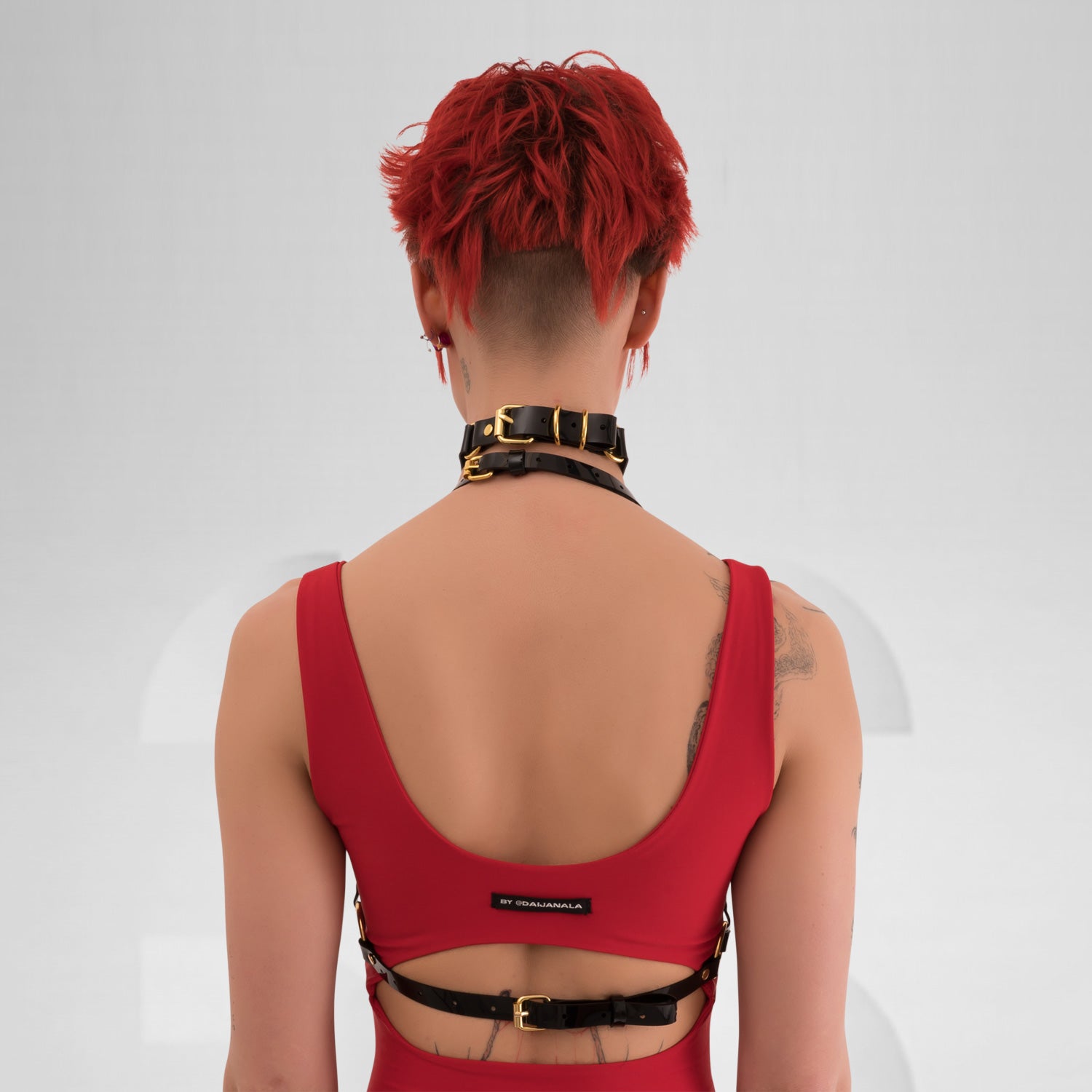  A back view of the Harness Top in Black PVC from Miss Overdose, featuring striking golden or silver rings. This edgy and stylish harness captures a kinky aesthetic, making it ideal for events, techno clubs, or festivals, while also ensuring a comfortable fit.