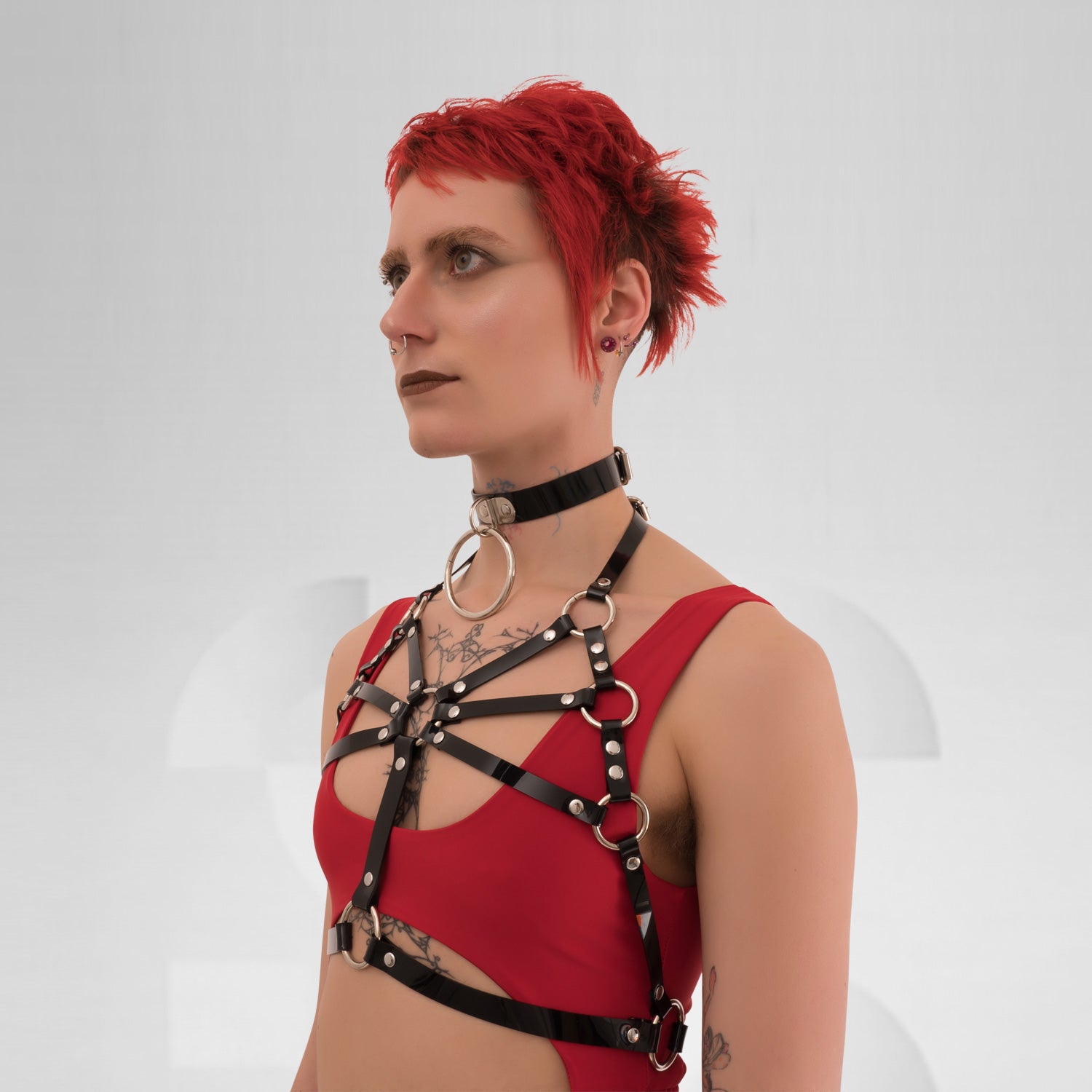  A back view of the Harness Top in Black PVC from Miss Overdose, featuring striking golden or silver rings. This edgy and stylish harness captures a kinky aesthetic, making it ideal for events, techno clubs, or festivals, while also ensuring a comfortable fit.