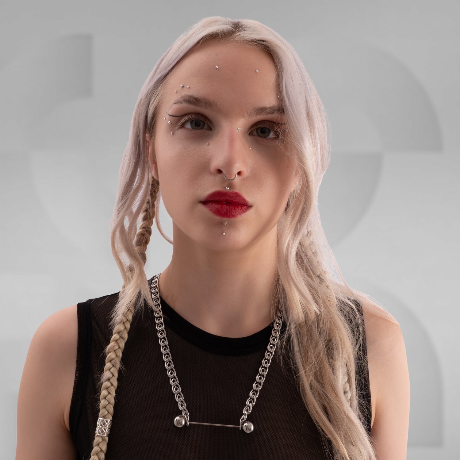 Close-up of a person wearing a bold industrial-style stainless steel chain necklace with thick, interlocking links and a unique barbell-inspired centerpiece. The necklace rests over a sheer black mesh top, complemented by platinum blonde braided hair for an edgy, avant-garde fashion look.