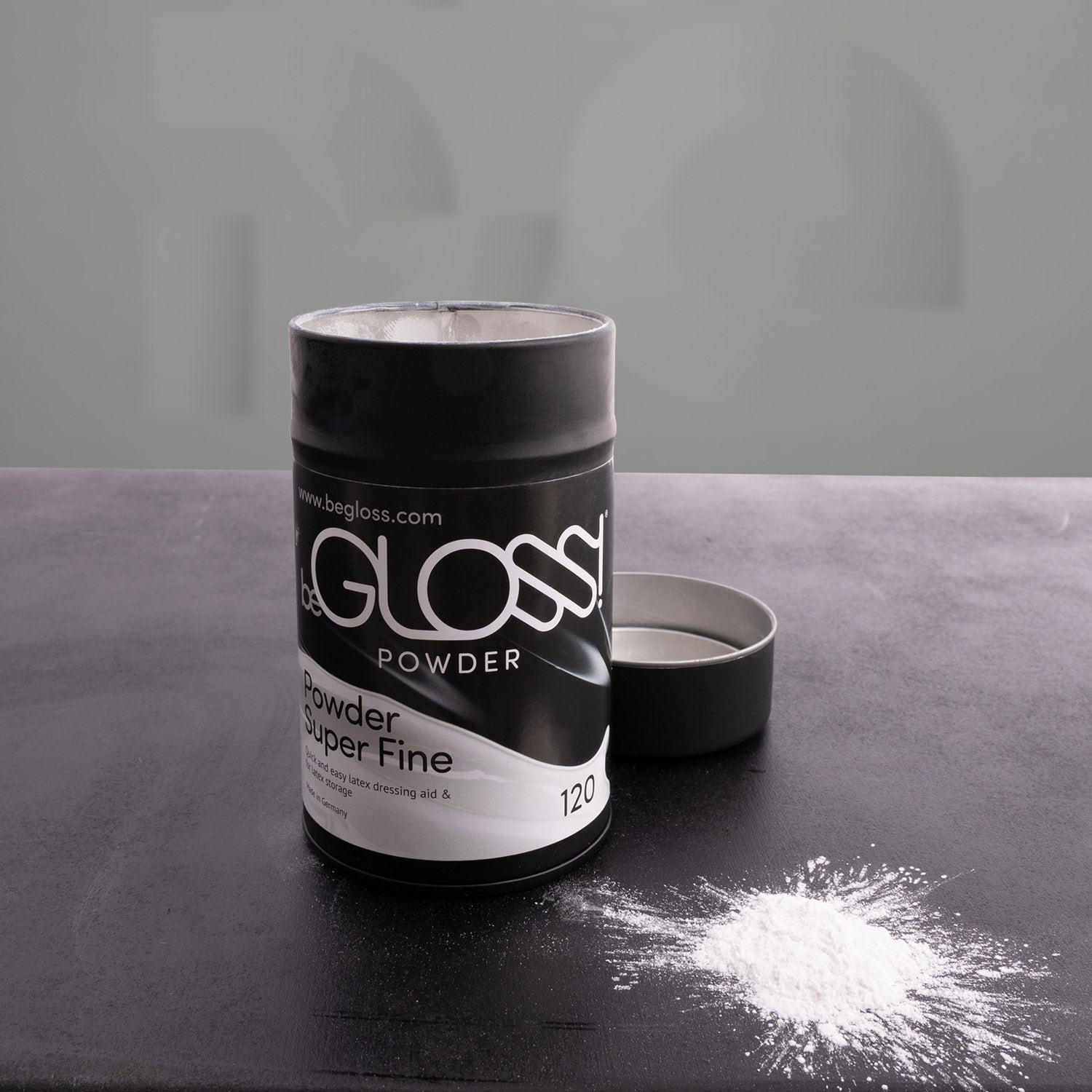 black latex poweder box open with poweer on table in front of grey background