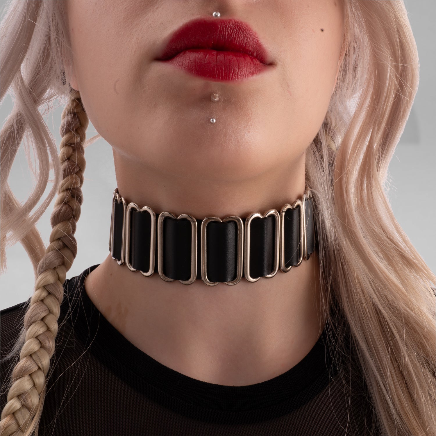The image features an avant-garde choker with rectangular black segments linked by metal hardware. It's a bold accessory that adds a unique, edgy touch to any look, blending modern elegance with a hint of rebellion.
