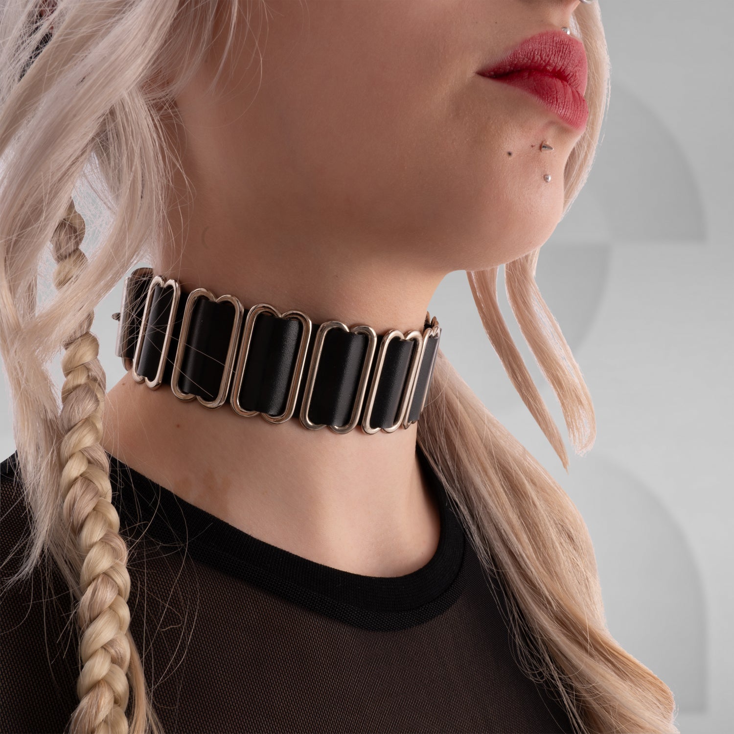 The image features an avant-garde choker with rectangular black segments linked by metal hardware. It's a bold accessory that adds a unique, edgy touch to any look, blending modern elegance with a hint of rebellion.