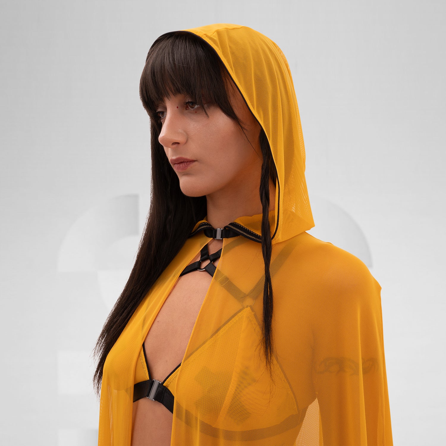 The image features a person wearing a flowing, sheer yellow cape that drapes elegantly to the floor. The cape is lightweight and creates a striking, dramatic silhouette. Underneath, the person is styled in minimal, edgy fashion, with strappy details adding a touch of avant-garde flair. The combination of the vibrant yellow cape and bold styling elements makes for a standout look that’s perfect for fashion-forward occasions.