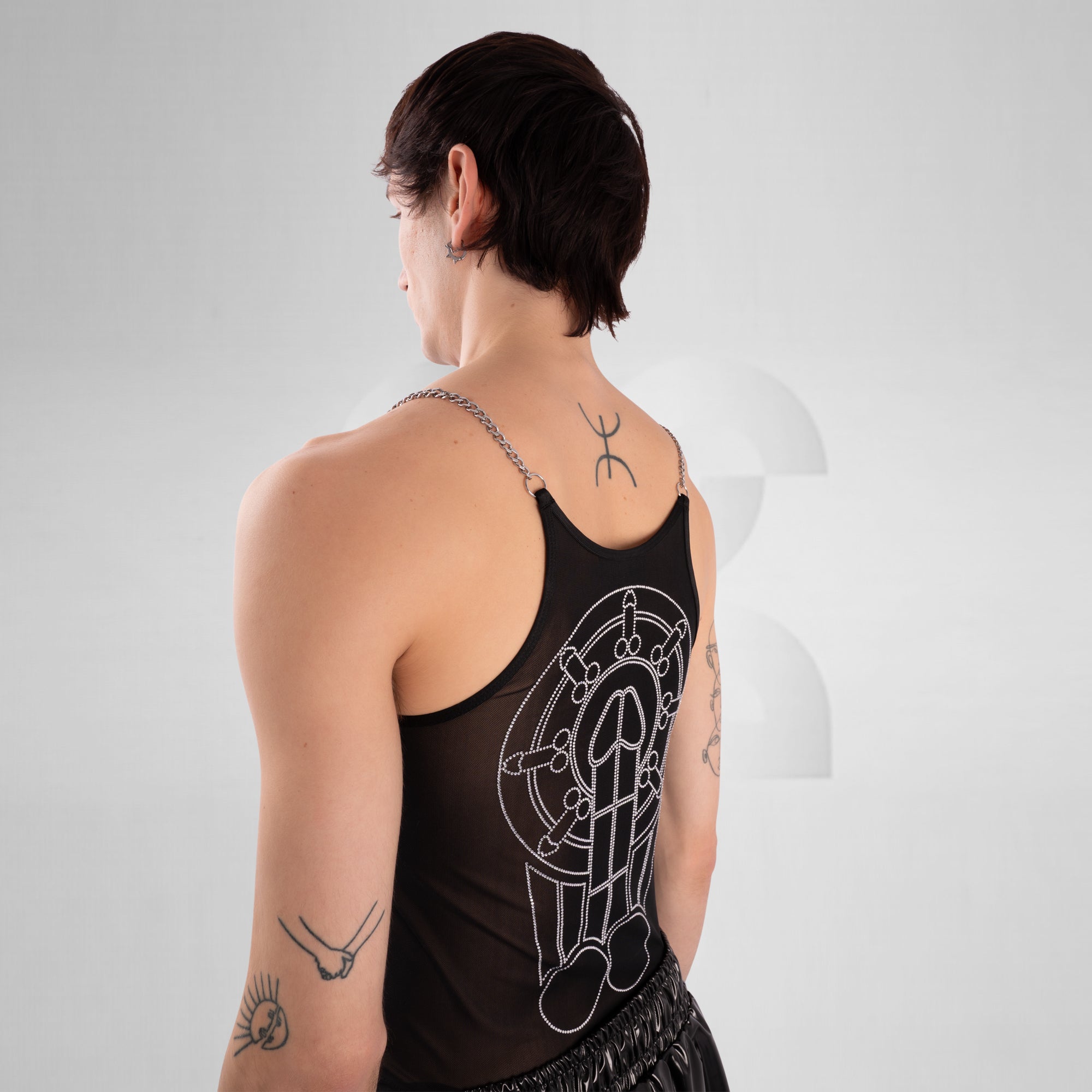Person wearing a black tank top with a geometric design, standing against a plain background