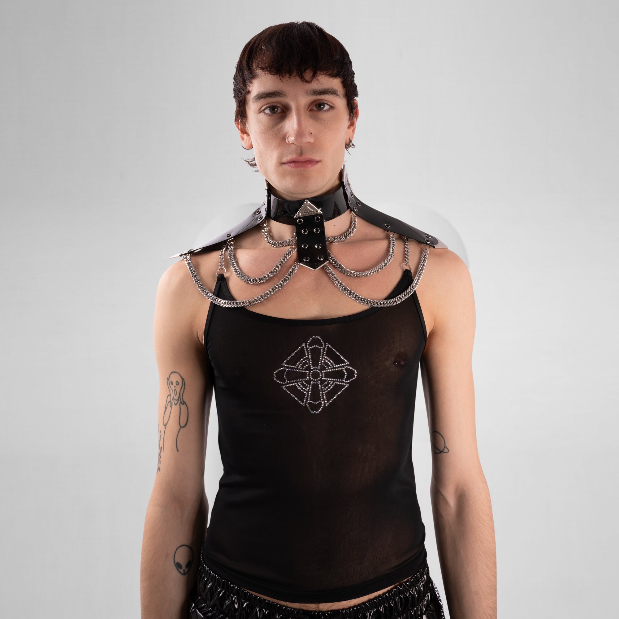 Person wearing a black top with intricate design and a decorative neckpiece on a plain background