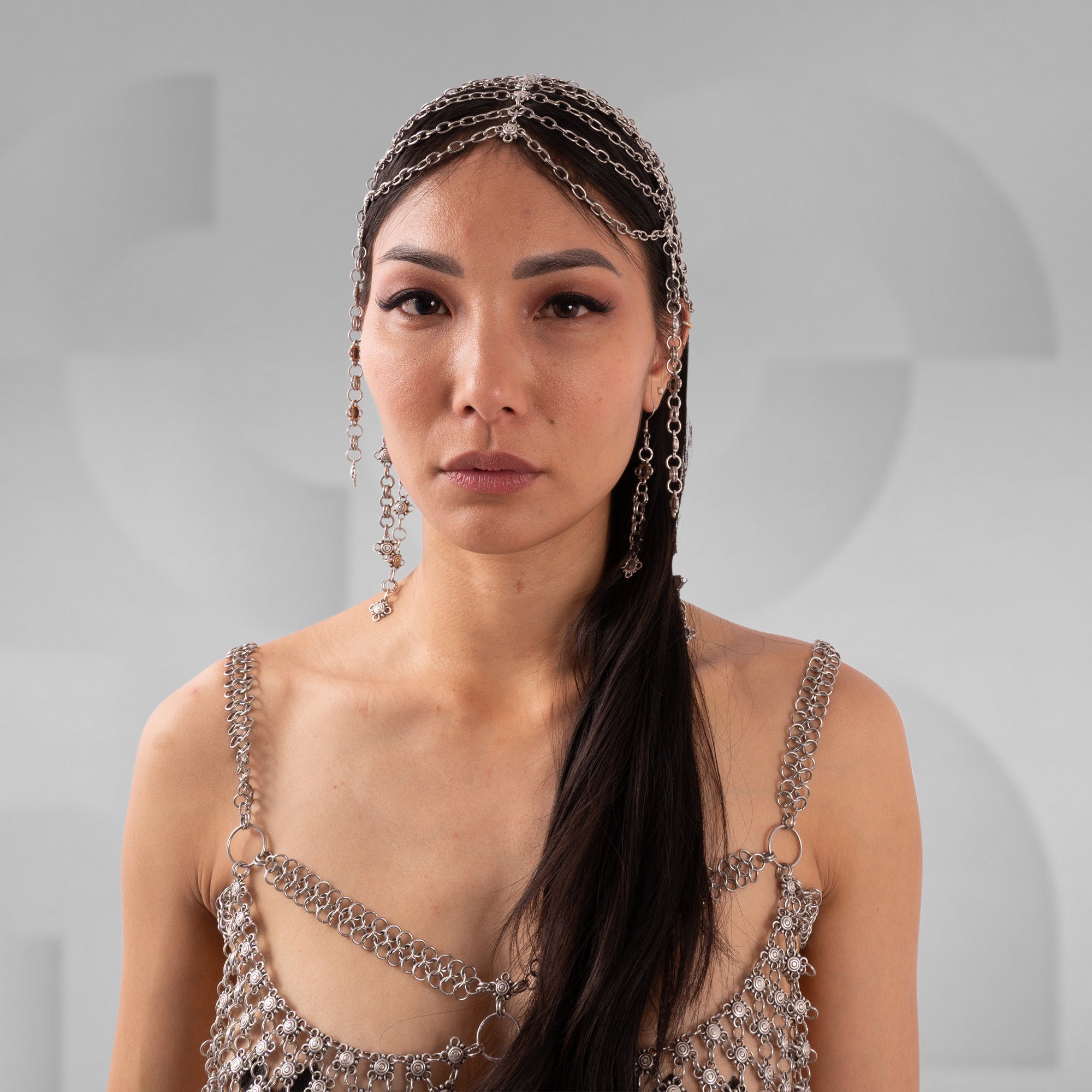 Woman wearing a decorative headpiece and dress with chain details against a gray background