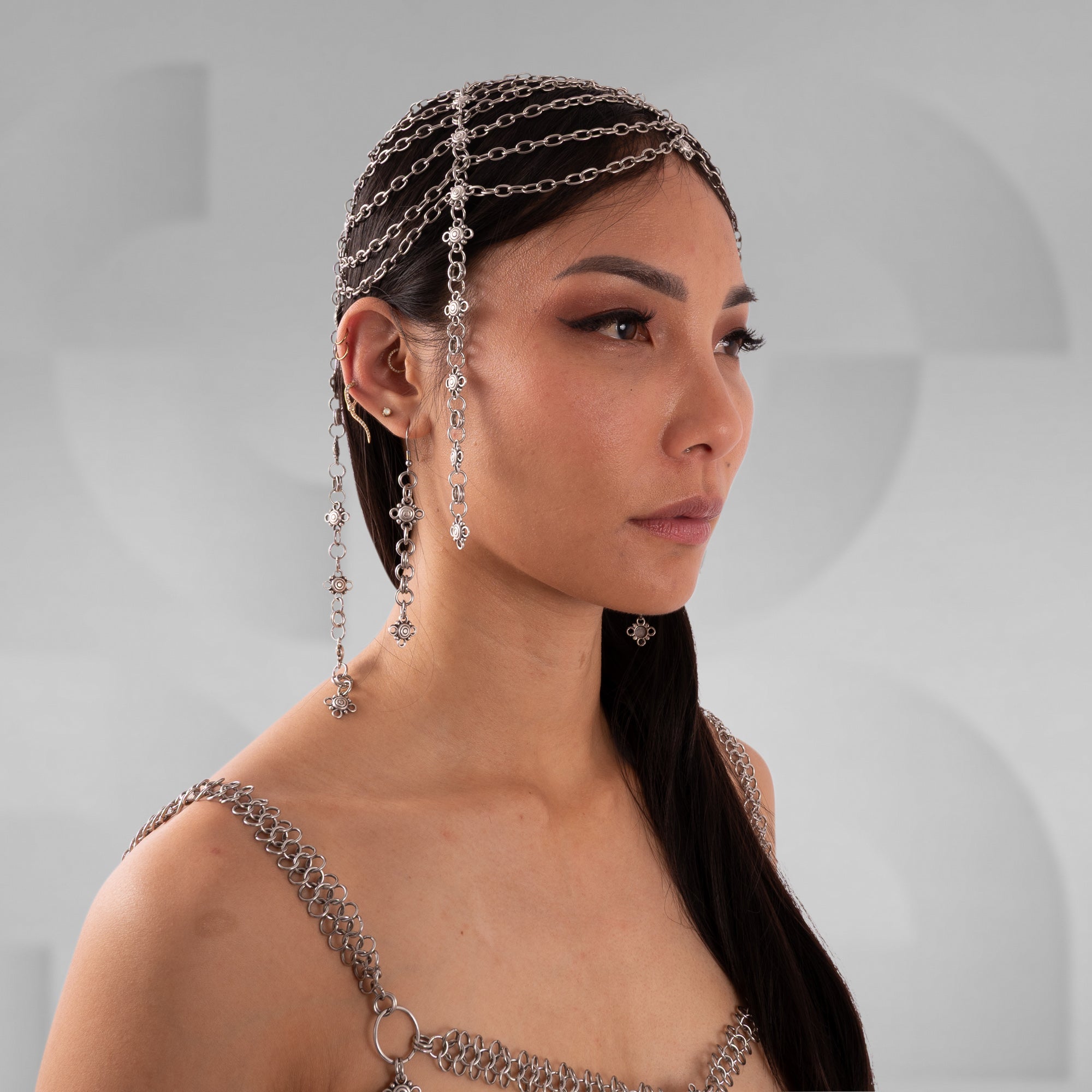 Woman wearing a chain headpiece and shoulder jewelry against a neutral background