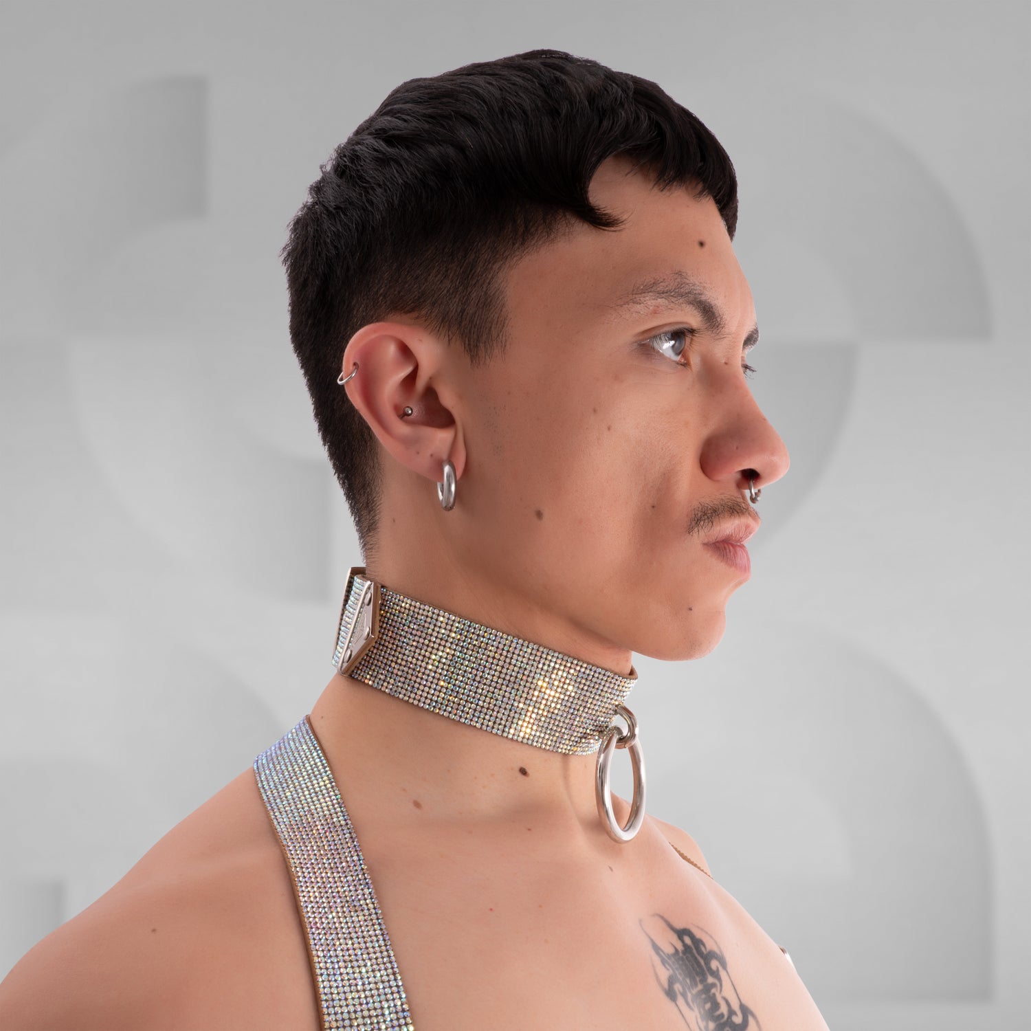 The image shows a close-up of a person wearing a sparkly choker with a large metallic ring in the center, complementing their bold tattoo. The choker has an eye-catching, glamorous design, making it a great accessory for standout fashion statements.