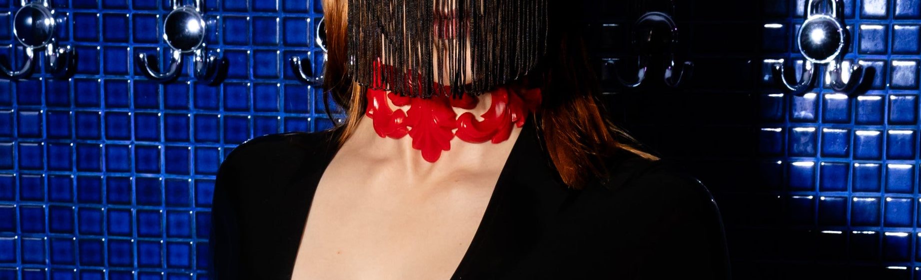 Person wearing a black latex outfit with red accents against a blue tiled wall.