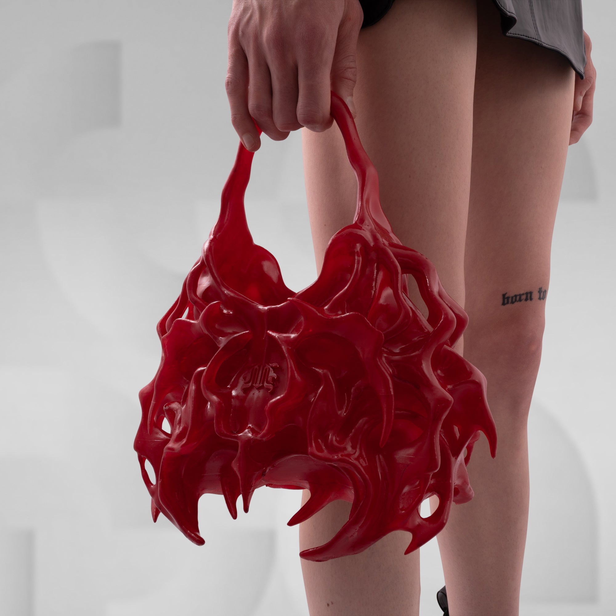 Person holding a red, abstract-shaped bag against a neutral background