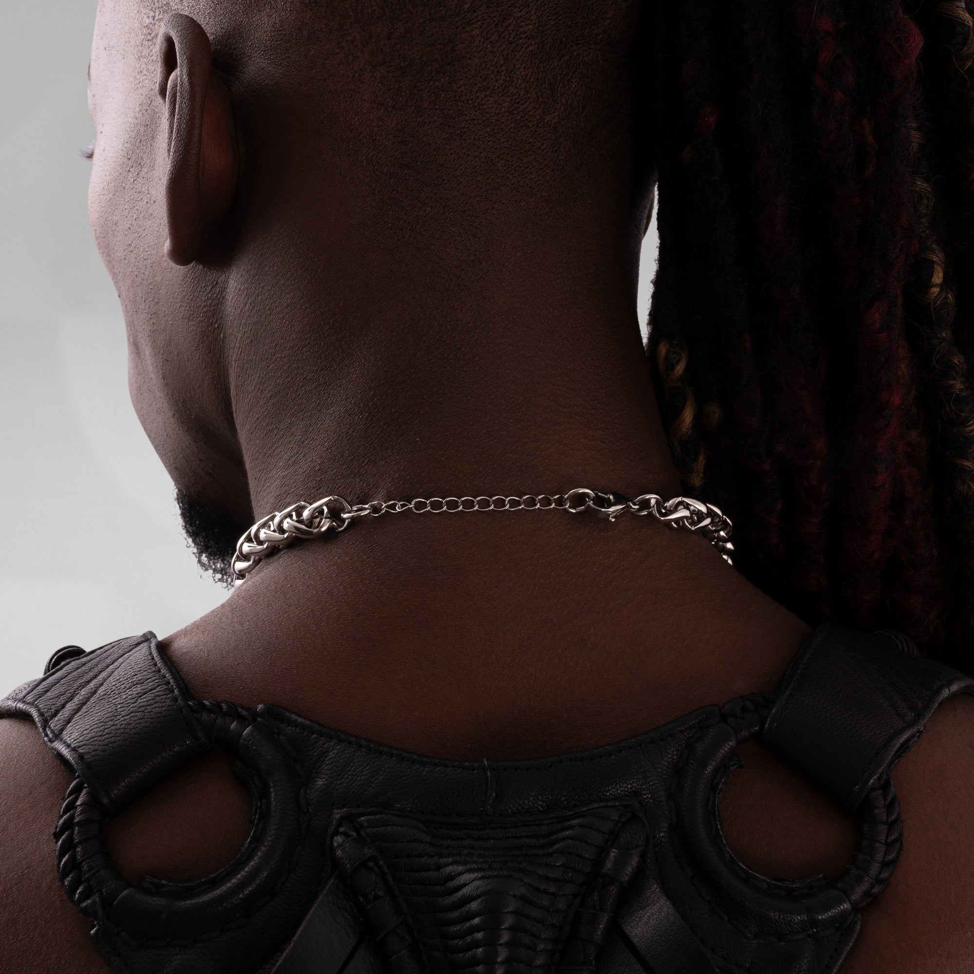 Person wearing a silver chain necklace with a plain background