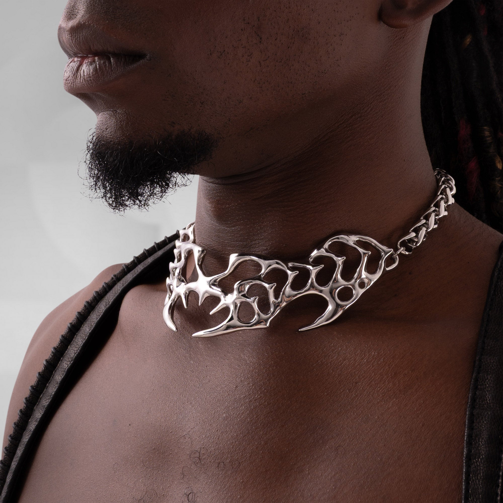 Man wearing a silver necklace with a detailed design on a neutral background