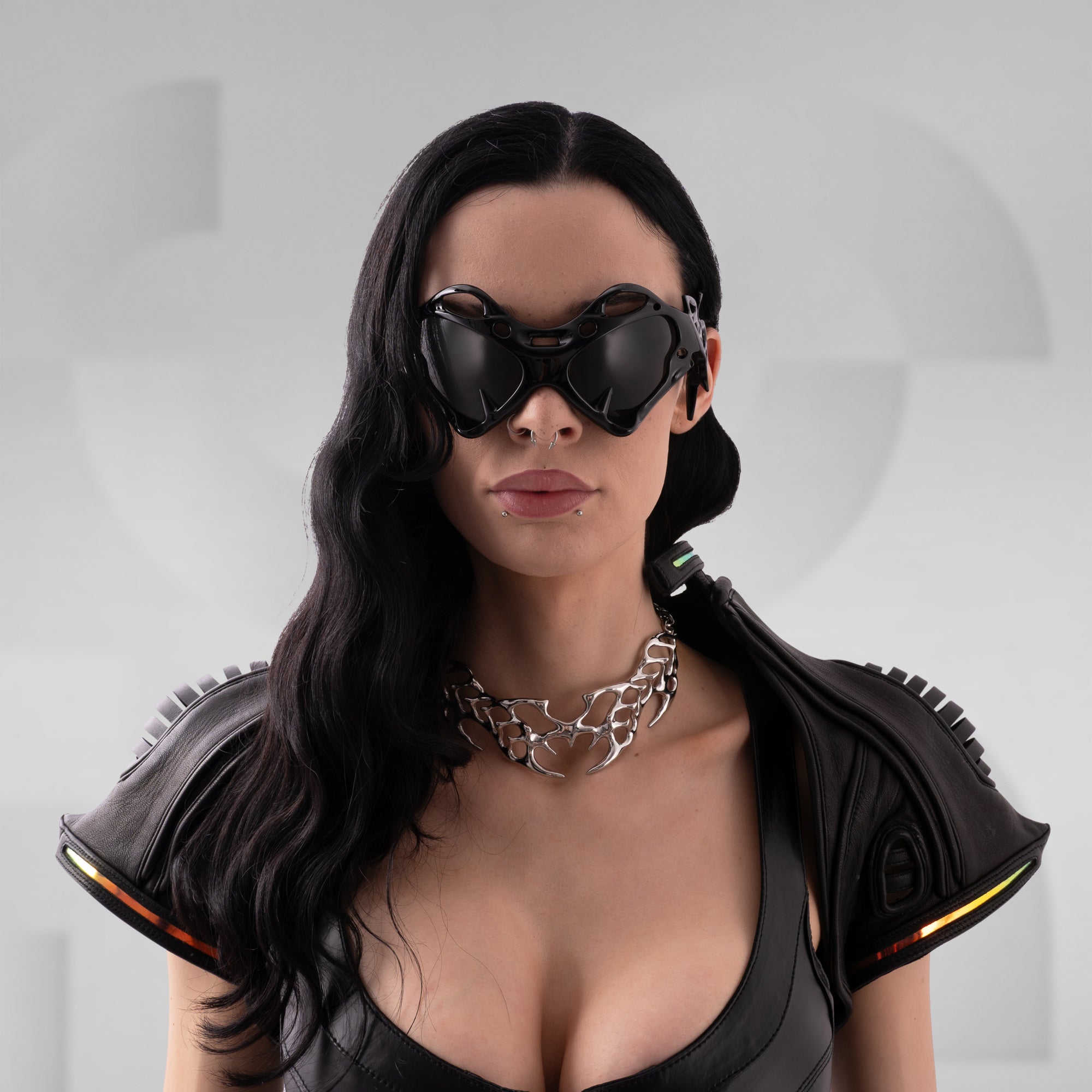 Person wearing futuristic goggles and black outfit with metallic accents on a gray background
