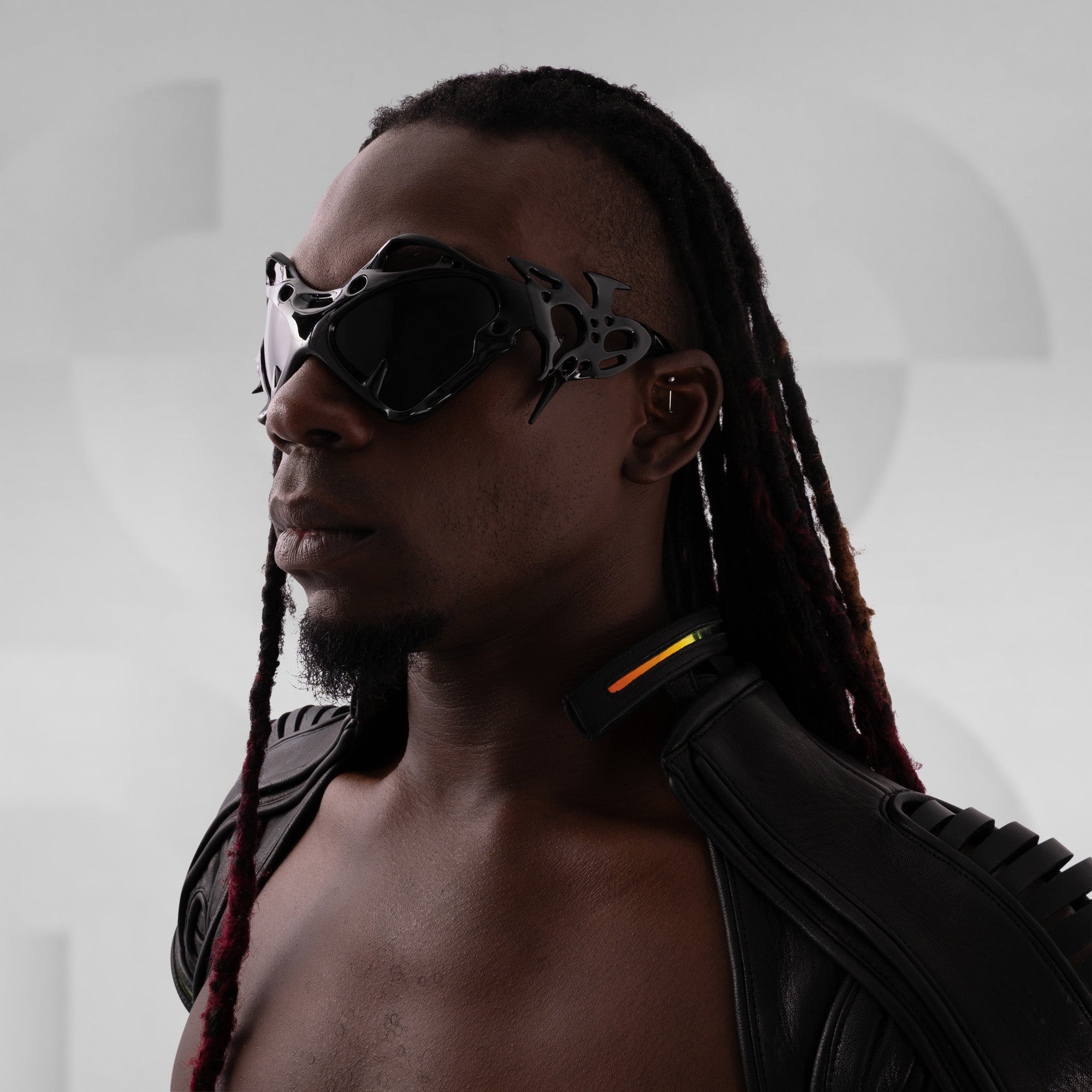 Person wearing futuristic sunglasses and a black leather outfit against a blurred background