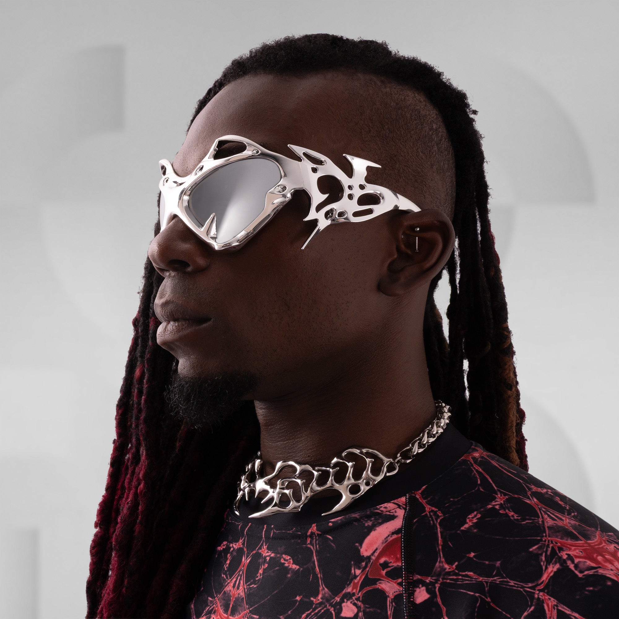Person wearing futuristic goggles with a red and black patterned shirt against a gray background