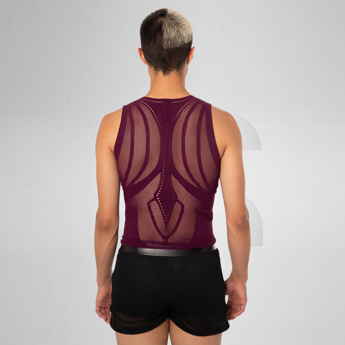 A man viewed from behind wearing a sleeveless, open-knit athletic tank top in deep burgundy and black shorts, set against a light gray studio background.