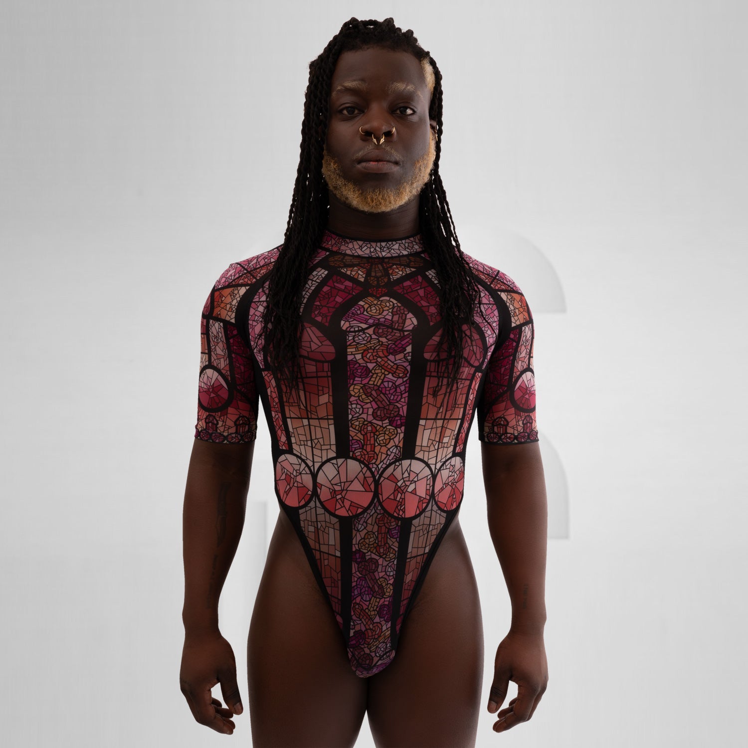 Guy stands with a mesh bodysuit in pink in front of a grey background