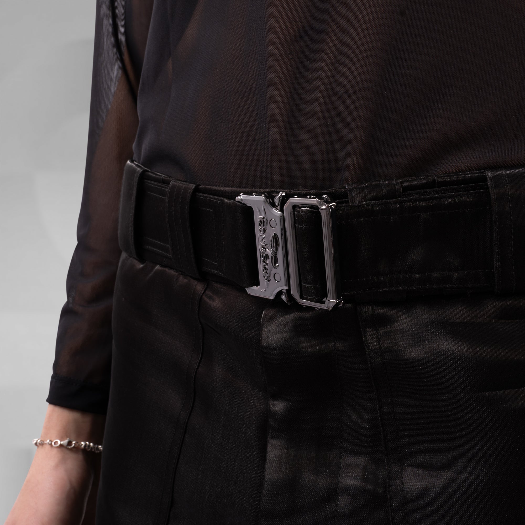 Person wearing a black belt with a silver buckle on a plain background