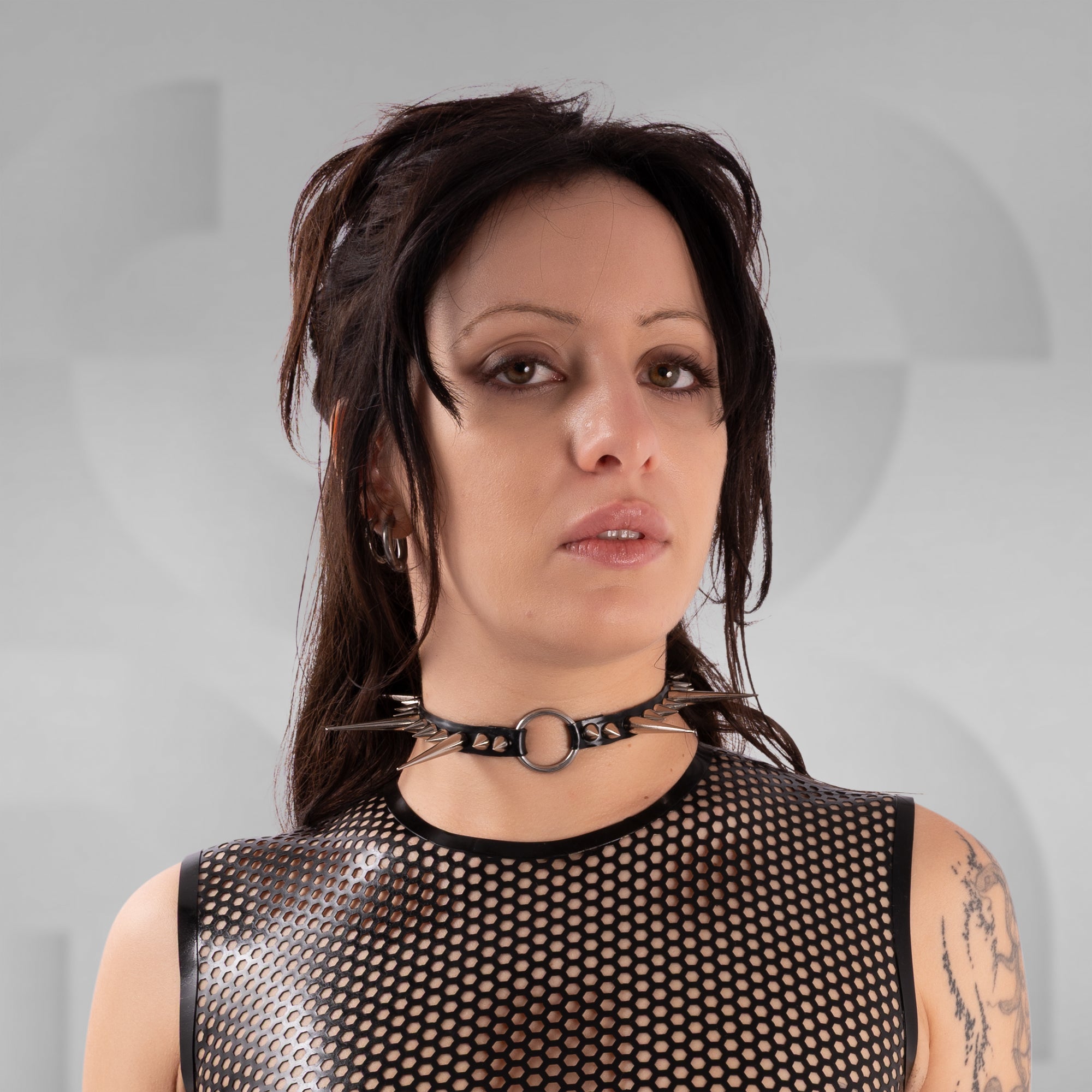 Woman wearing a black mesh top and choker against a gray background