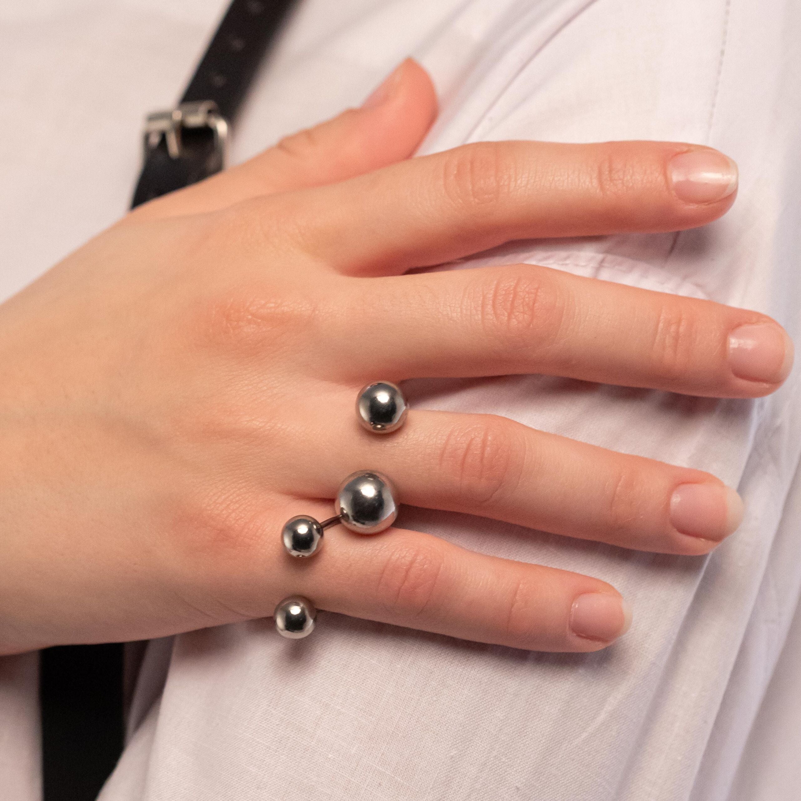 A person's hand showcasing a silver-colored ring with multiple balls, positioned on the ring finger.