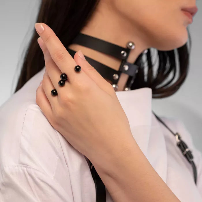 A close-up image of a person's hand wearing a black adjustable ring with black balls, on a chain necklace.