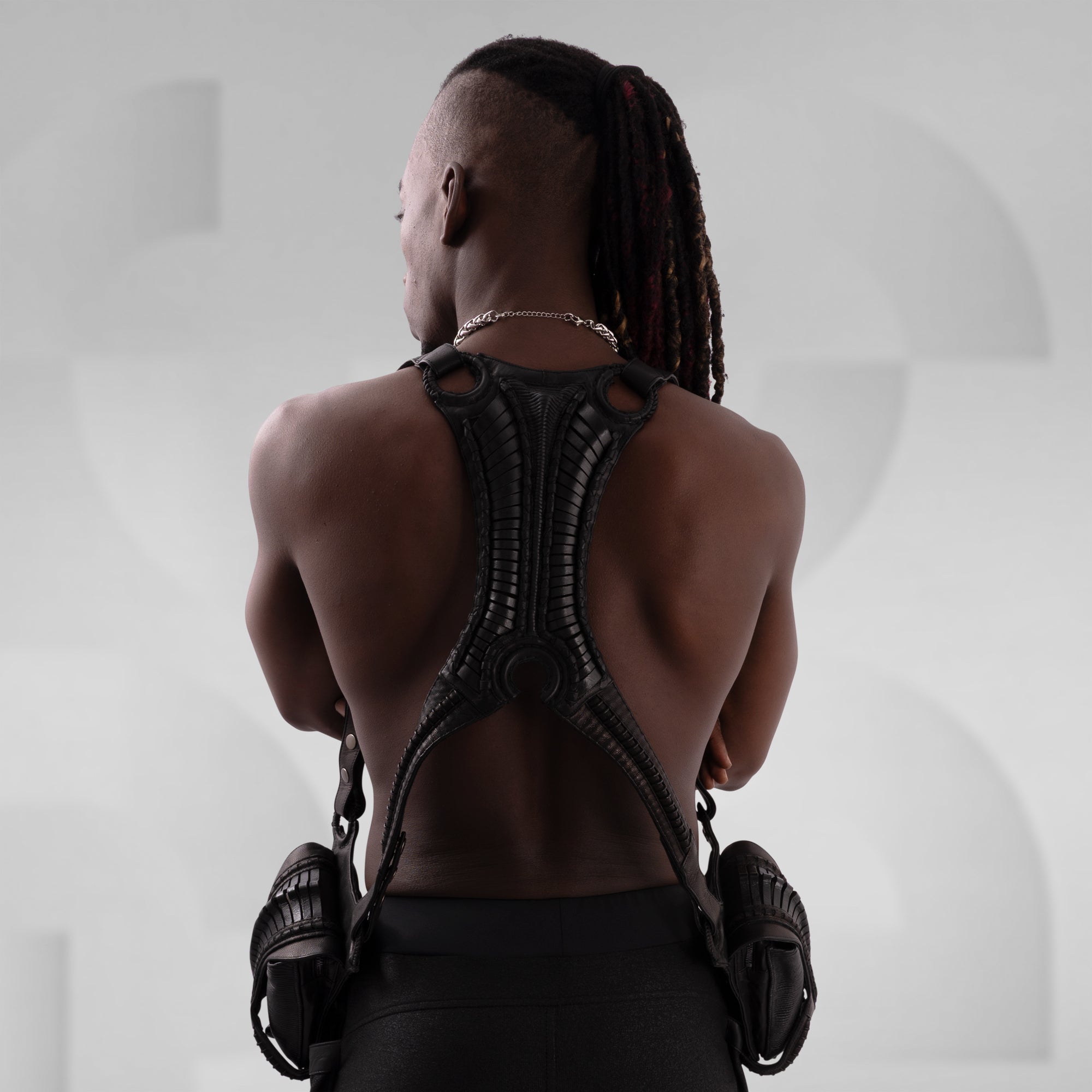 Person wearing a black, intricate backpiece against a neutral background