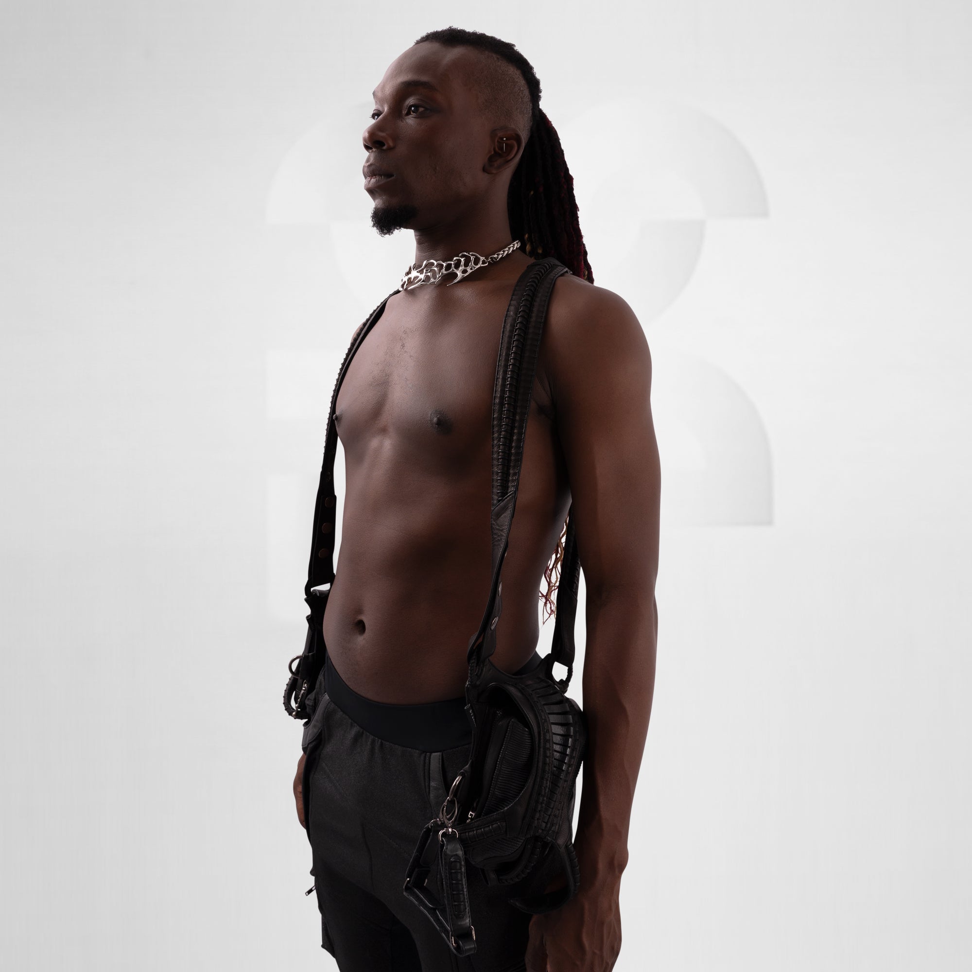 Man with dreadlocks wearing a black leather harness against a white background