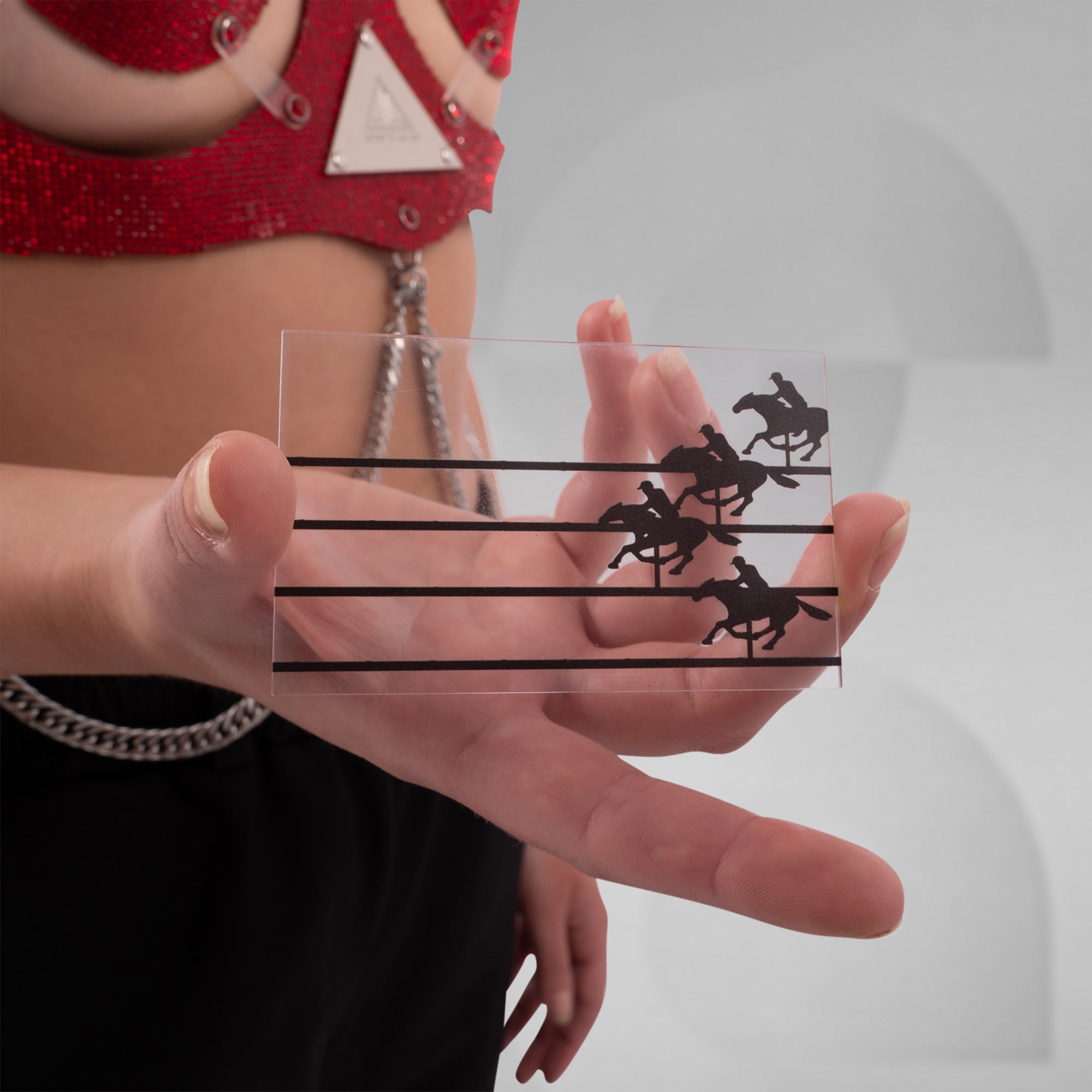Person holding a transparent card with horse racing illustrations against a blurred background