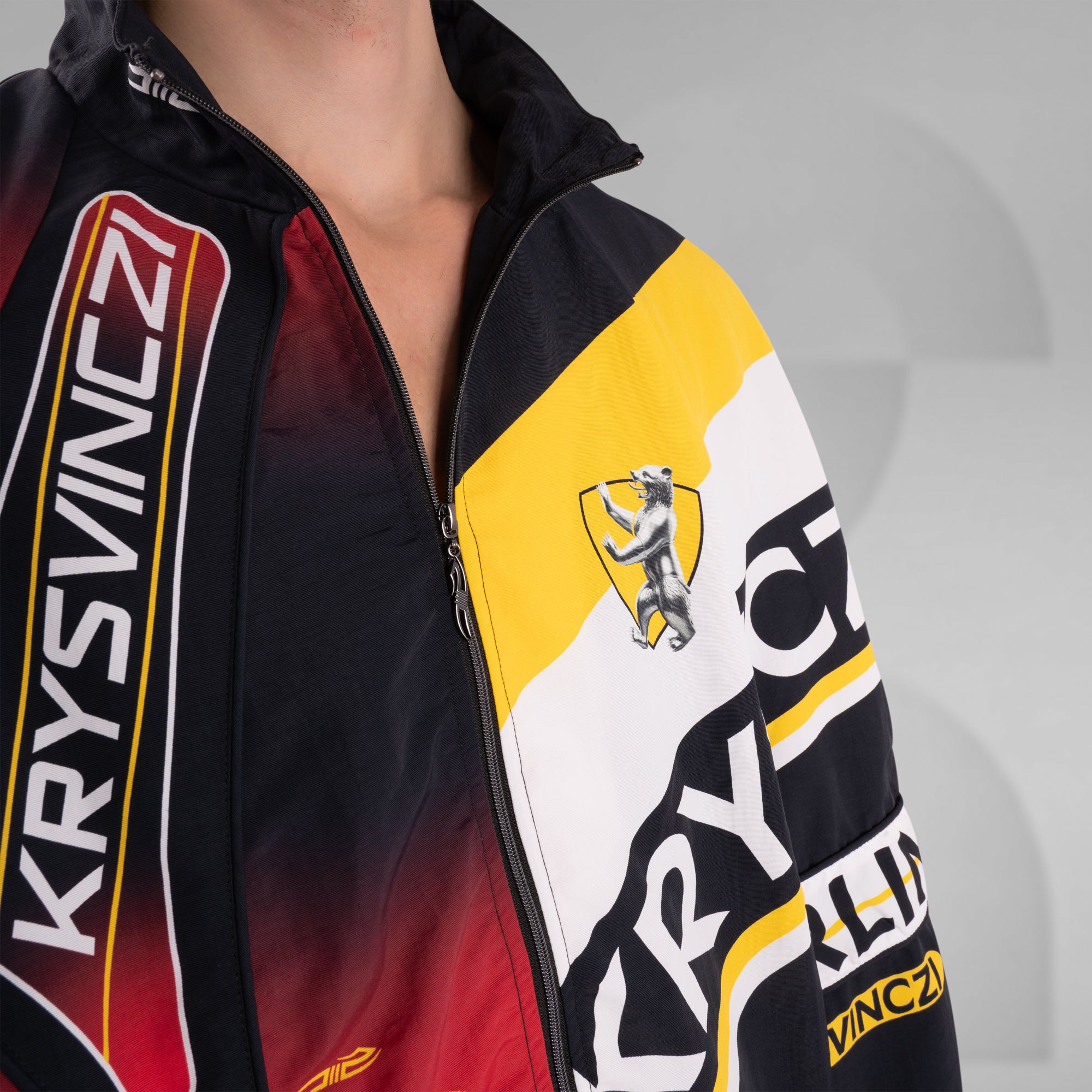 Close-up of a jacket with KRYSVINCZI branding and a logo on a gray background
