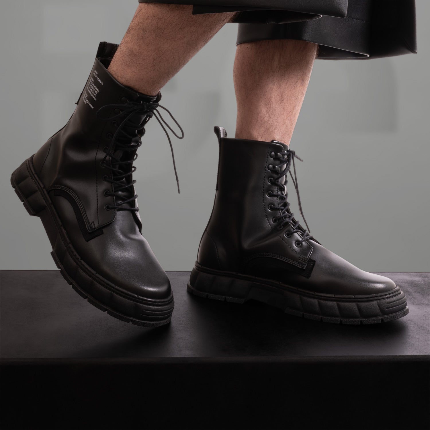 The image showcases a pair of striking black combat boots, featuring a modern twist on classic design. With a chunky sole and sleek leather finish, these boots exude an edgy vibe perfect for the fashion-forward individual. The bold lacing adds a rugged yet stylish touch, making them ideal for both urban adventures and clubwear. An essential addition to any avant-garde wardrobe!