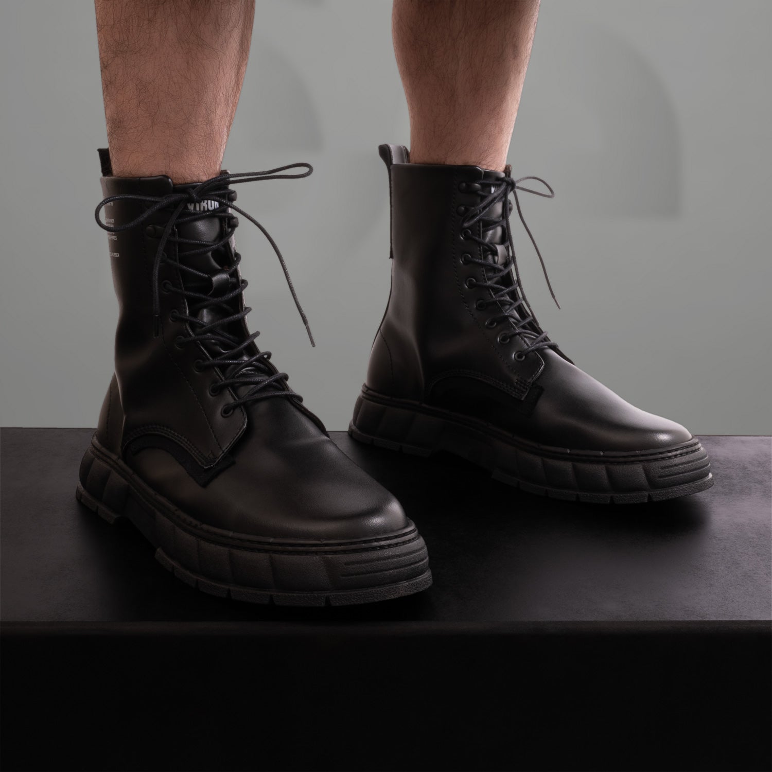The image showcases a pair of striking black combat boots, featuring a modern twist on classic design. With a chunky sole and sleek leather finish, these boots exude an edgy vibe perfect for the fashion-forward individual. The bold lacing adds a rugged yet stylish touch, making them ideal for both urban adventures and clubwear. An essential addition to any avant-garde wardrobe!