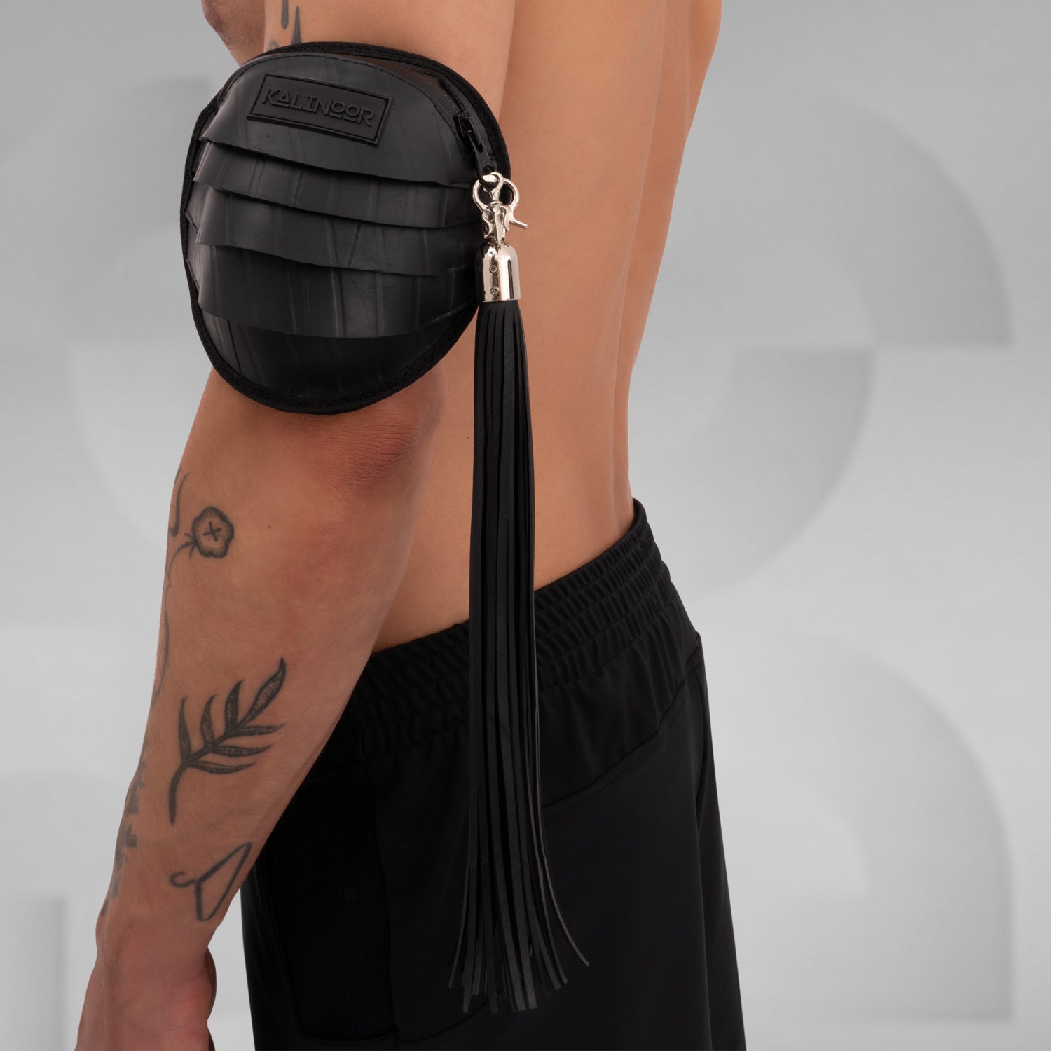 Side view of a black rubber whip accessory with metal clasp, attached to an arm pouch, designed to be clipped onto a fan or other accessories for added flair in clubwear.