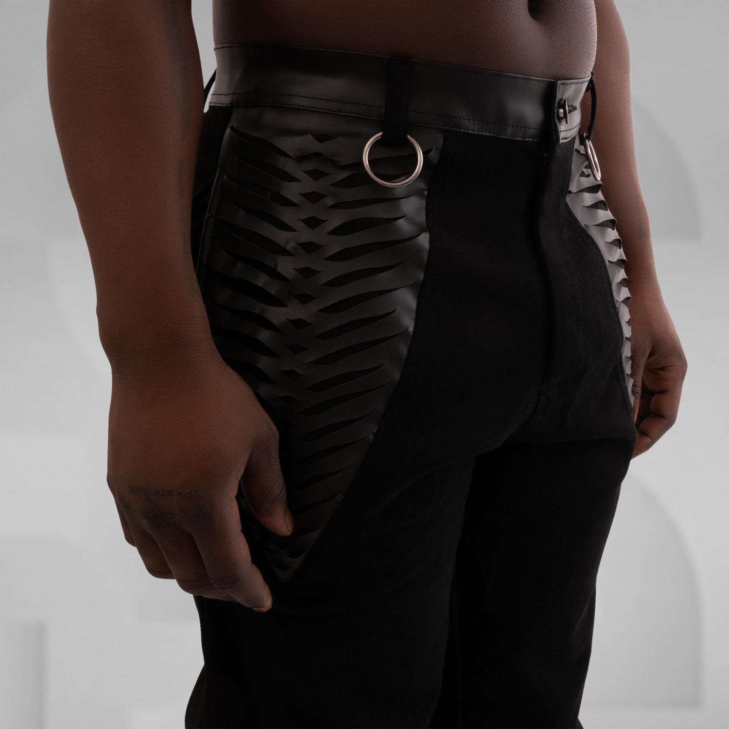 Black jeans with intricate vegan leather laser cut pockets and silver ring accents for a trendy and edgy look.