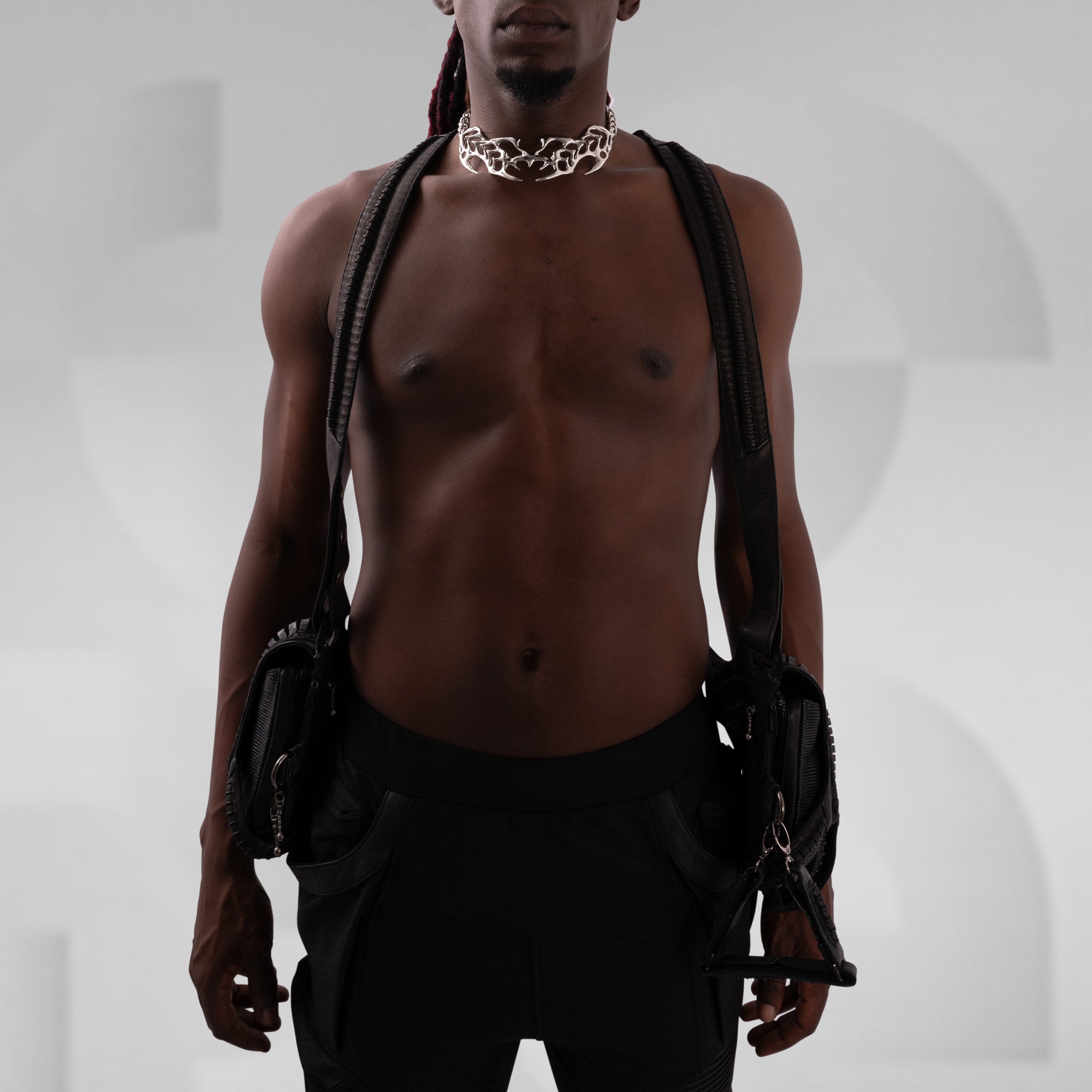 Man with a gold chain necklace and black leather gloves against a gray background