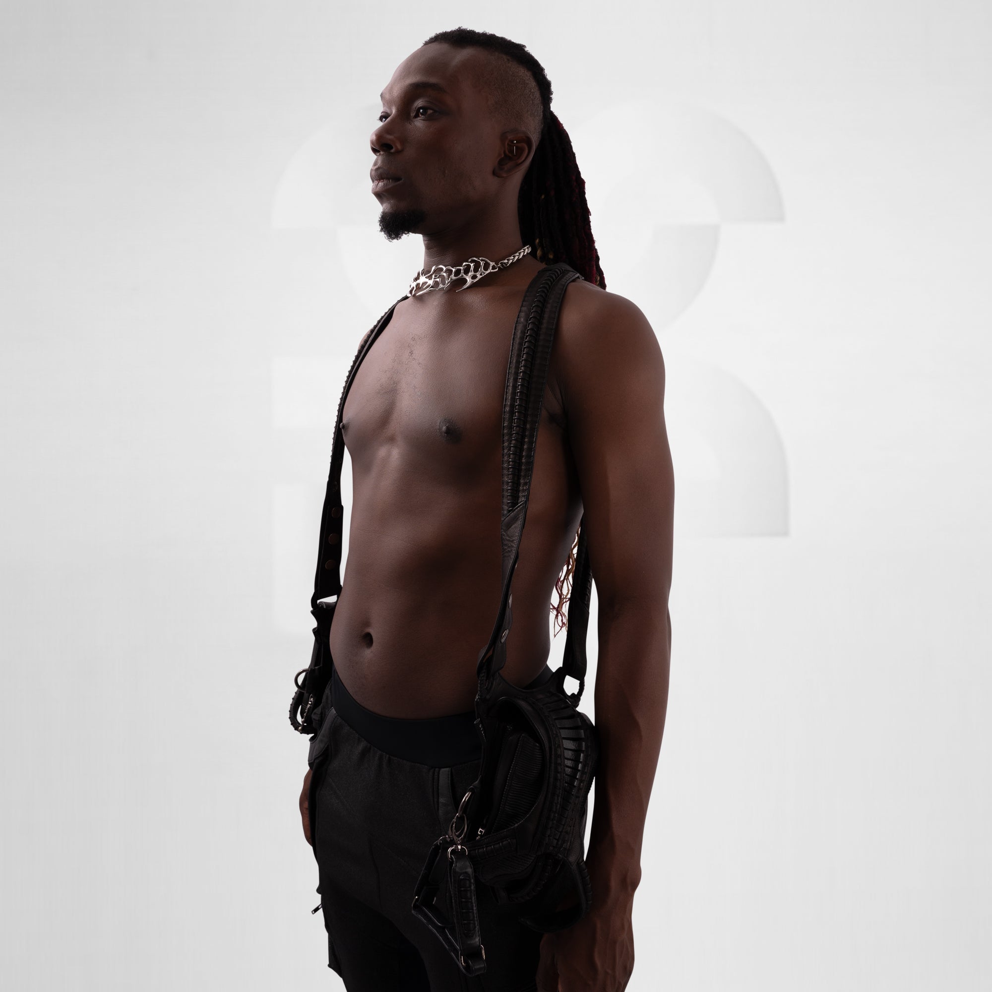 Man with dreadlocks wearing a leather harness against a white background