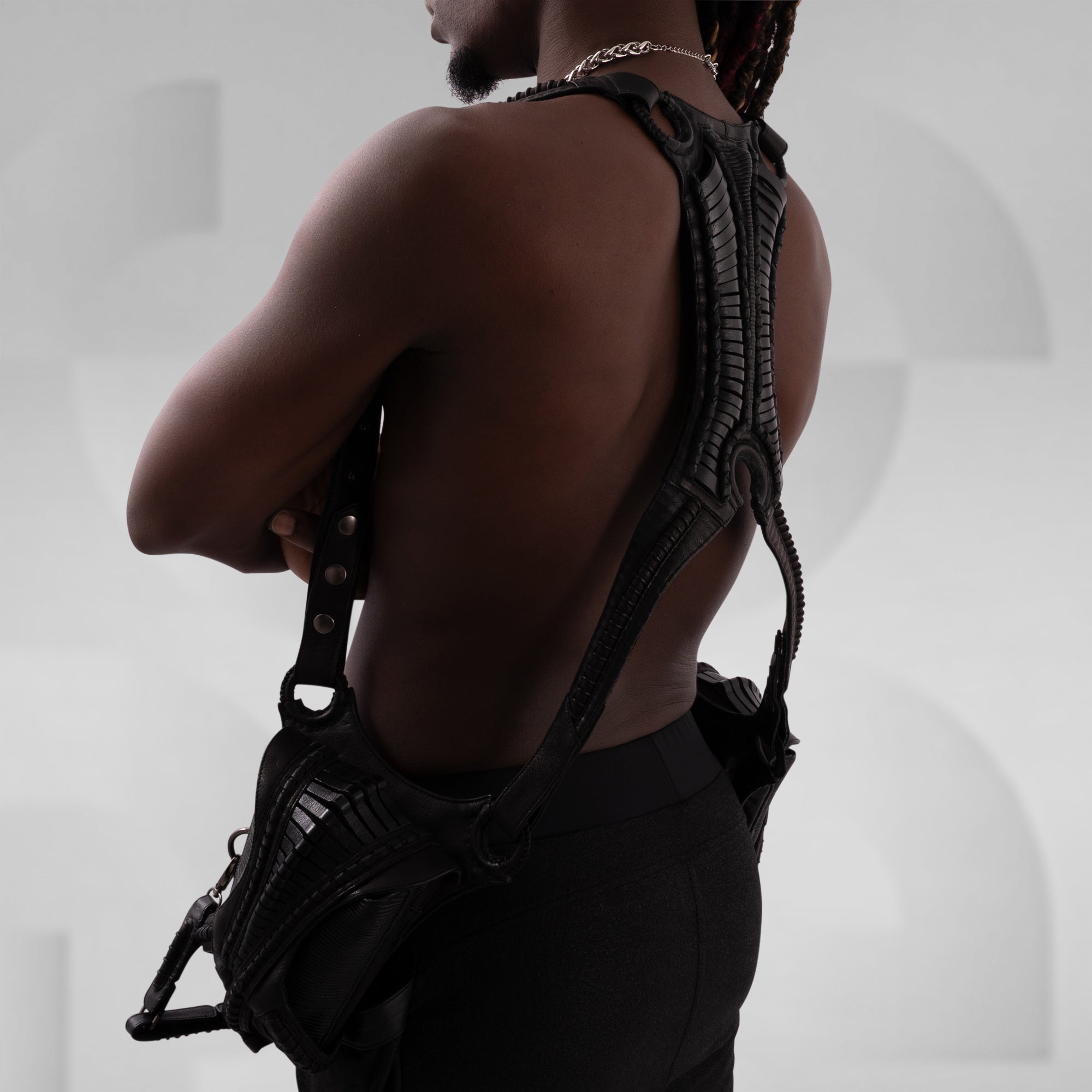 Person wearing a black harness against a neutral background