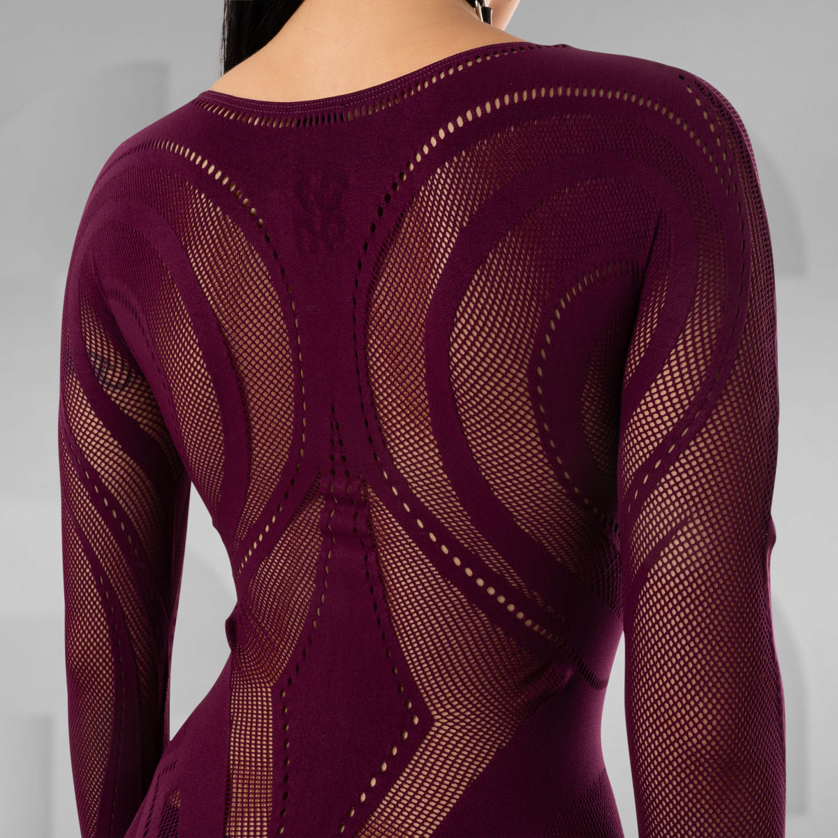 A close-up back view of a model wearing a long-sleeve knit top in deep burgundy with an intricate openwork geometric pattern.