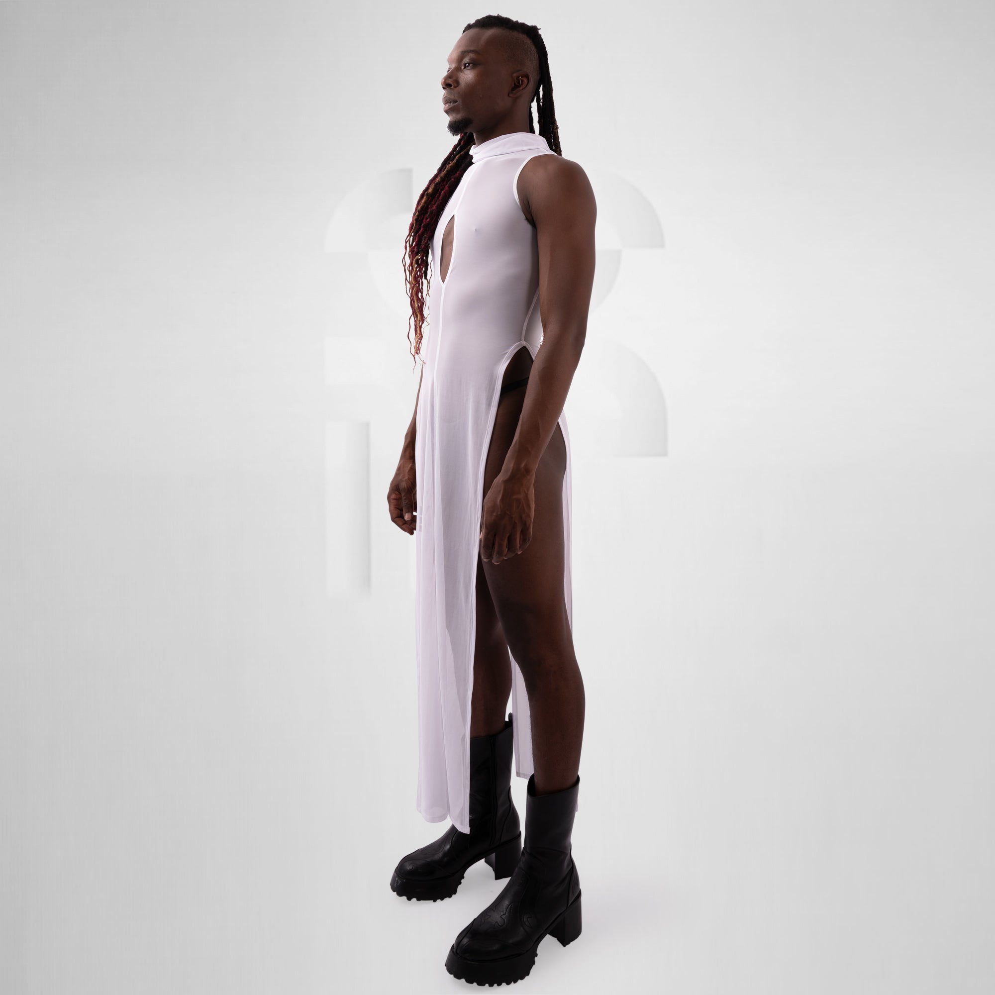 Person wearing a white sleeveless dress with a high slit and black boots on a plain background